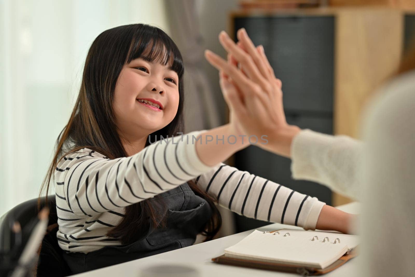 Happy little cute girl finish schoolwork giving high five to mother. Distance education, homeschooling concept.