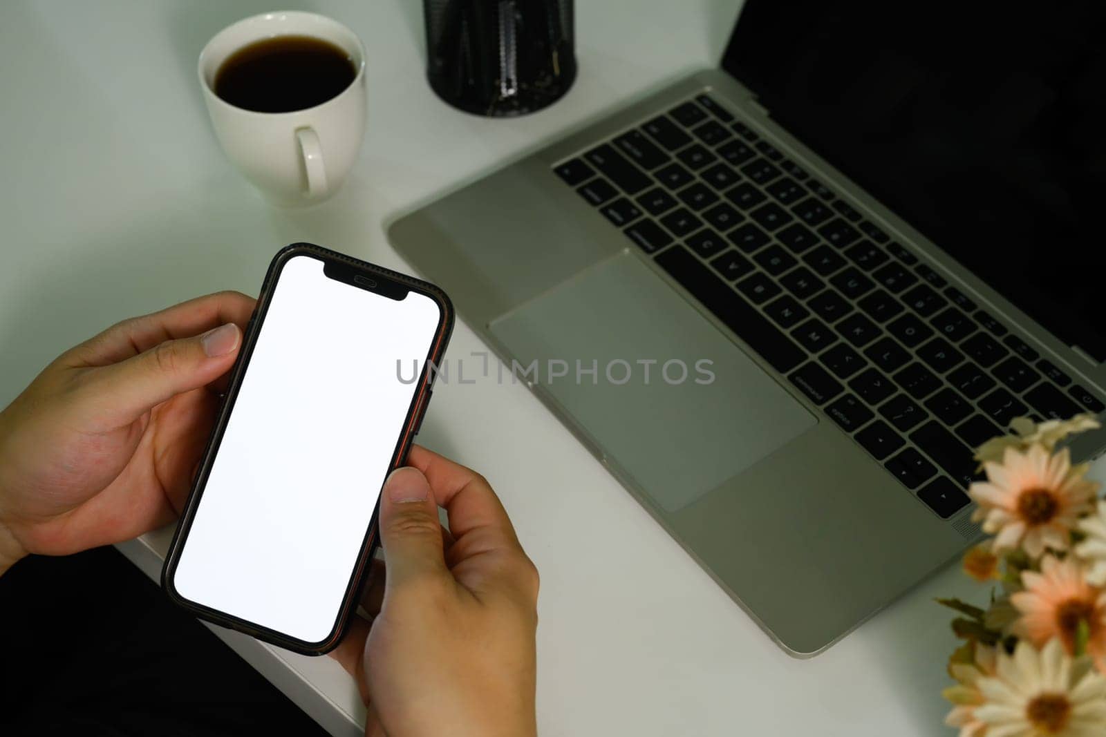 Closeup view of man sitting at office desk with laptop and using smartphone. Blank screen your advertising text message.