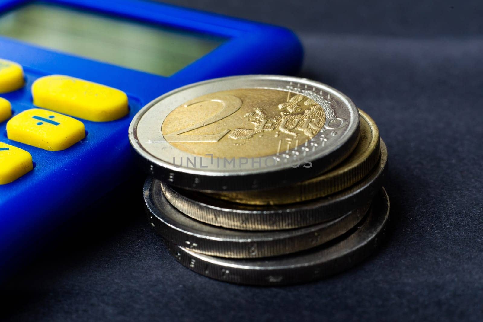Money concept. Blue calculator with coins euro, close up, dark black background