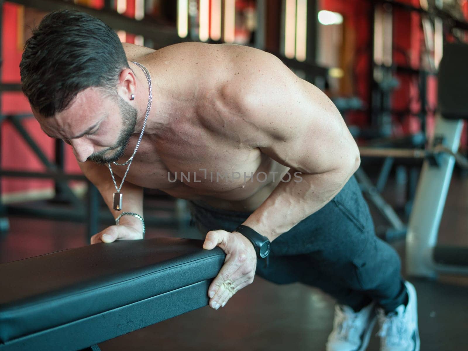 Attractive and fit young man in gym working out pecs and exercising on equipment, on a bench