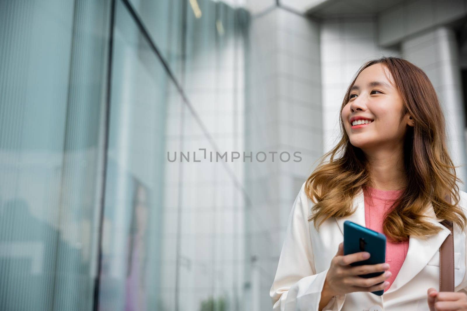 Asian businesswoman texting smartphone commuting work she walking near her office building in morning, Beautiful business woman smiling hold mobile phone outdoor walking on city street urban