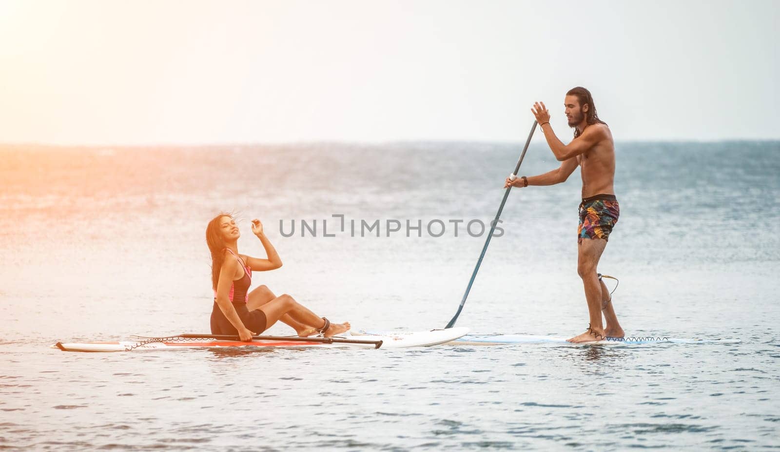 Sea woman and man on sup. Silhouette of happy young woman and man, surfing on SUP board, confident paddling through water surface. Idyllic sunset. Active lifestyle at sea or river