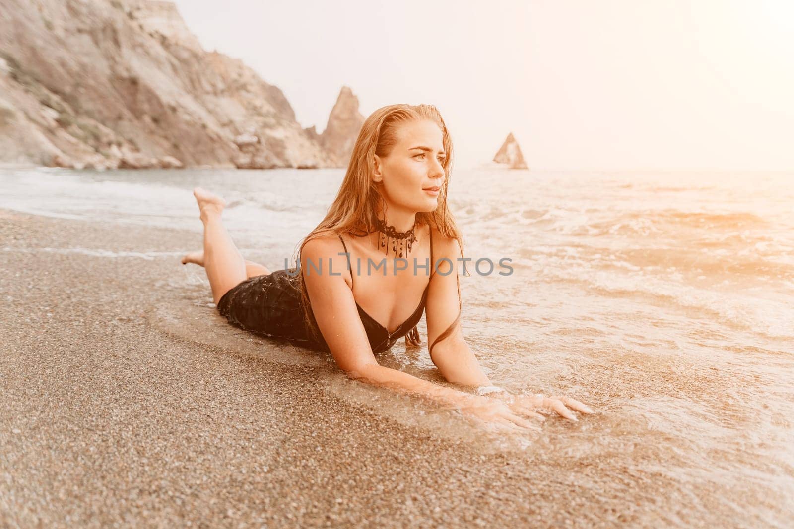 Woman summer travel sea. Happy tourist in black dress enjoy taking picture outdoors for memories. Woman traveler posing on sea beach surrounded by volcanic mountains, sharing travel adventure journey by panophotograph