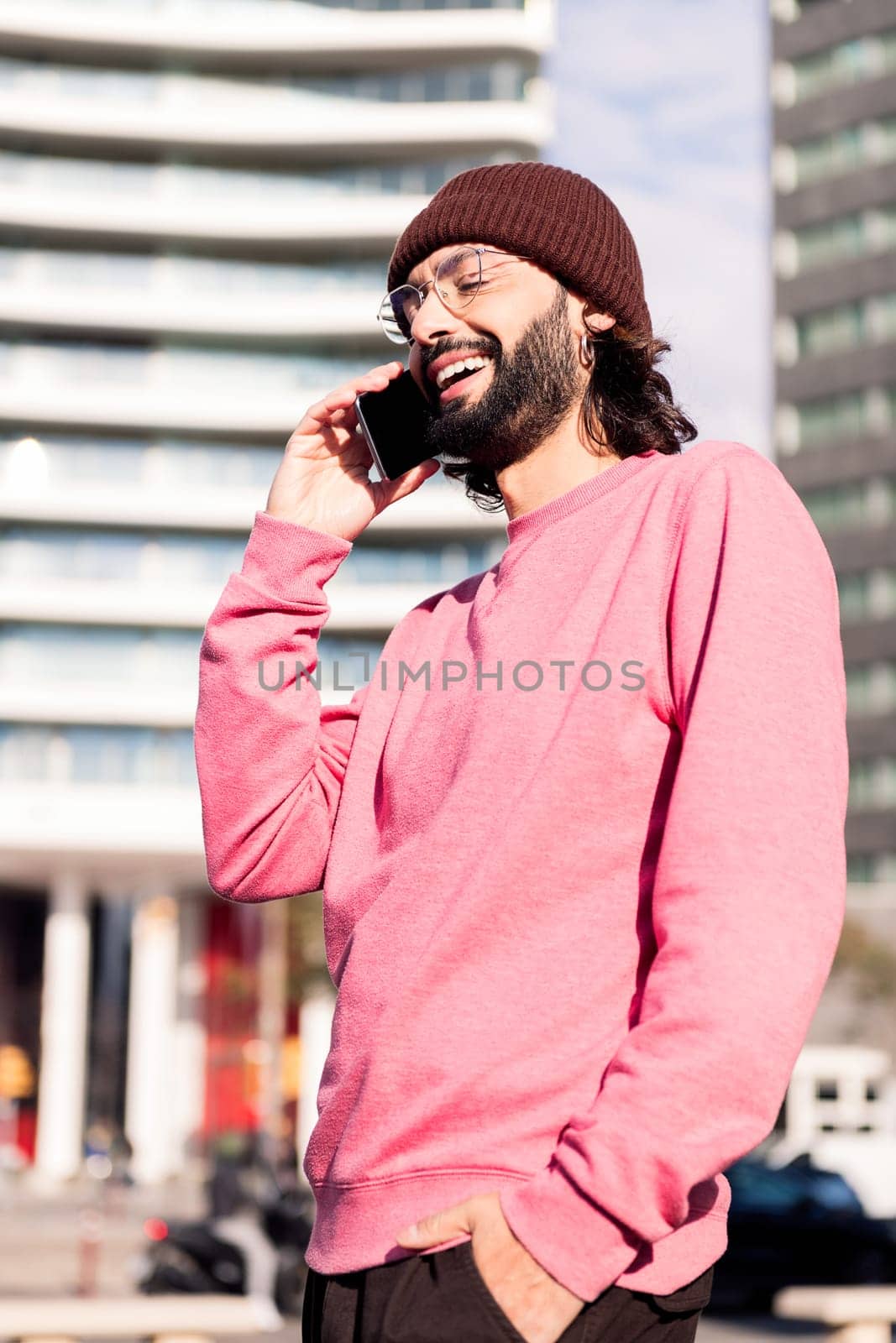 laughing young man on phone during sunny city walk, concept of urban lifestyle and technology of communication
