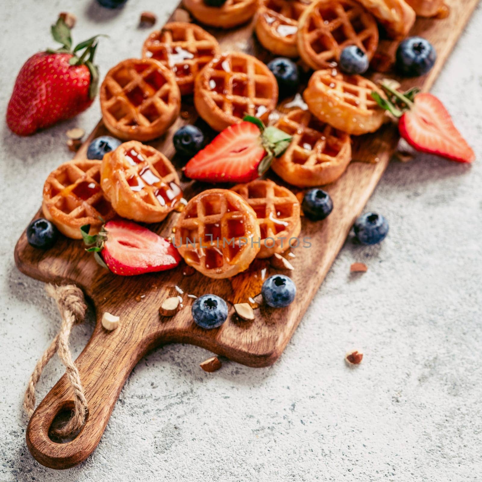 Small round delicious soft belgian waffles on cutting board. Fresh belgian waffles with berries and caramel sauce top view. Copy space for text or mock up. Square. Toned imege