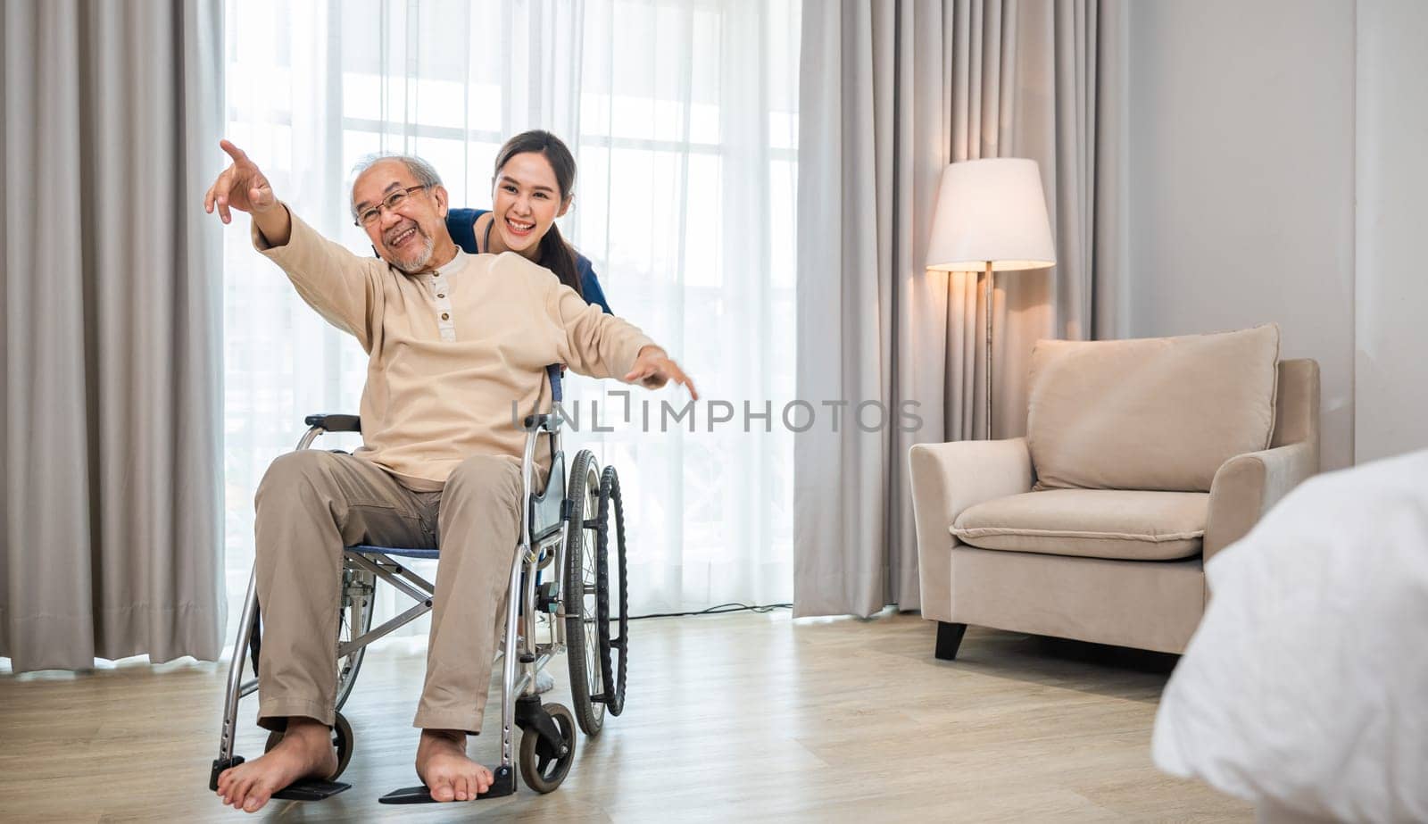 senior retired old man sitting on wheelchair having fun with young woman nurse by Sorapop