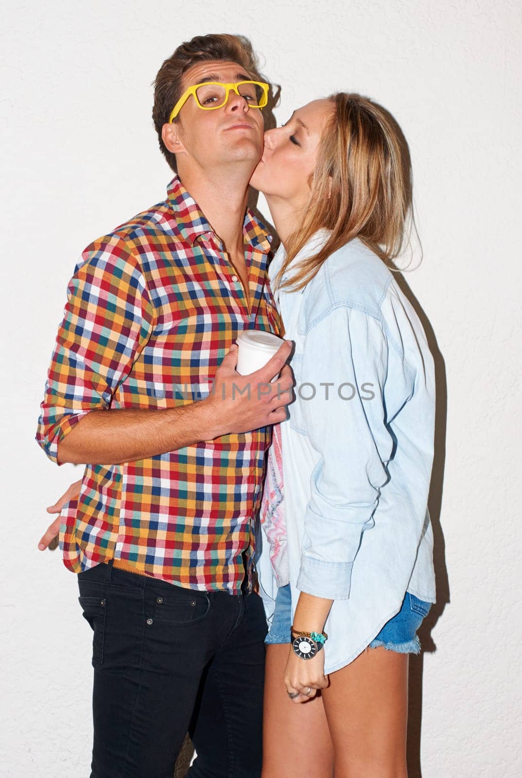 Kiss, portrait of hipster couple with coffee drink and glasses in gen z fashion with university culture in youth. Happiness, woman and man in kissing at college, cool kids on white wall background