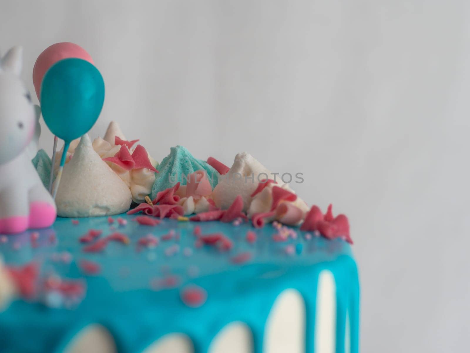 studio shot of chocolate frosted blue dripped icing white cup cake, unicorn , meringue and sprinkles on top