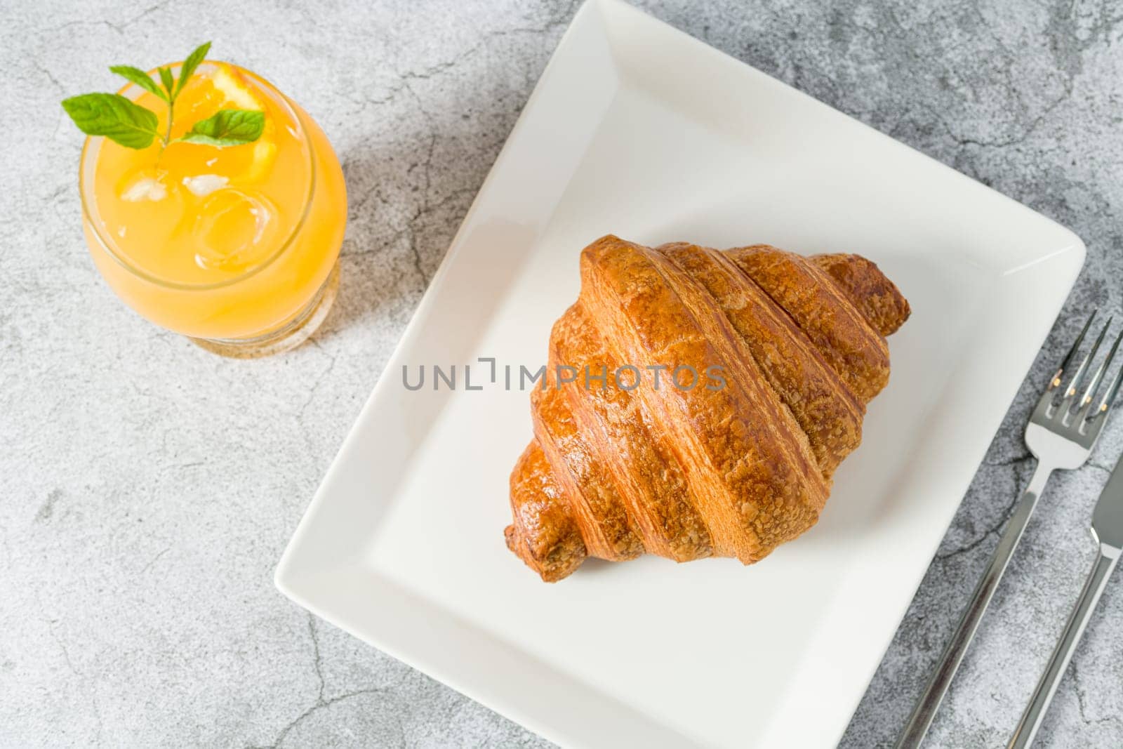 Croissant on a white porcelain plate with freshly squeezed orange juice on the side