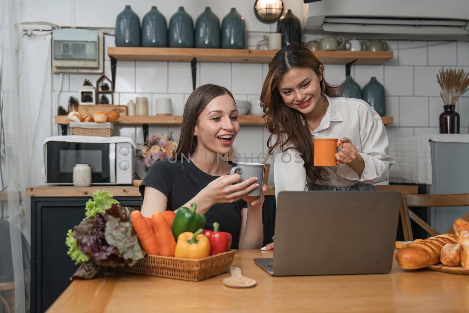 Two beautiful woman friends having breakfast and drinking coffee while talking in the kitchen at home.