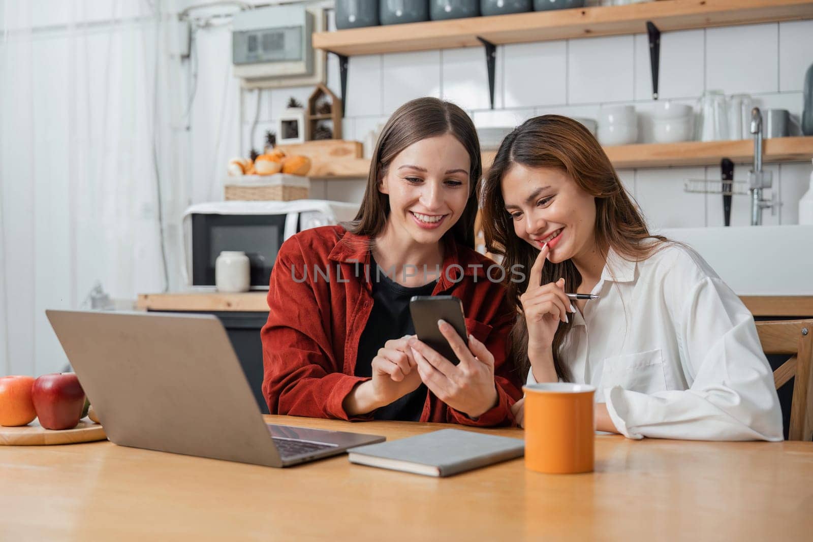 Two teenage girls are happy to receive messages from phone, social media in the kitchen.