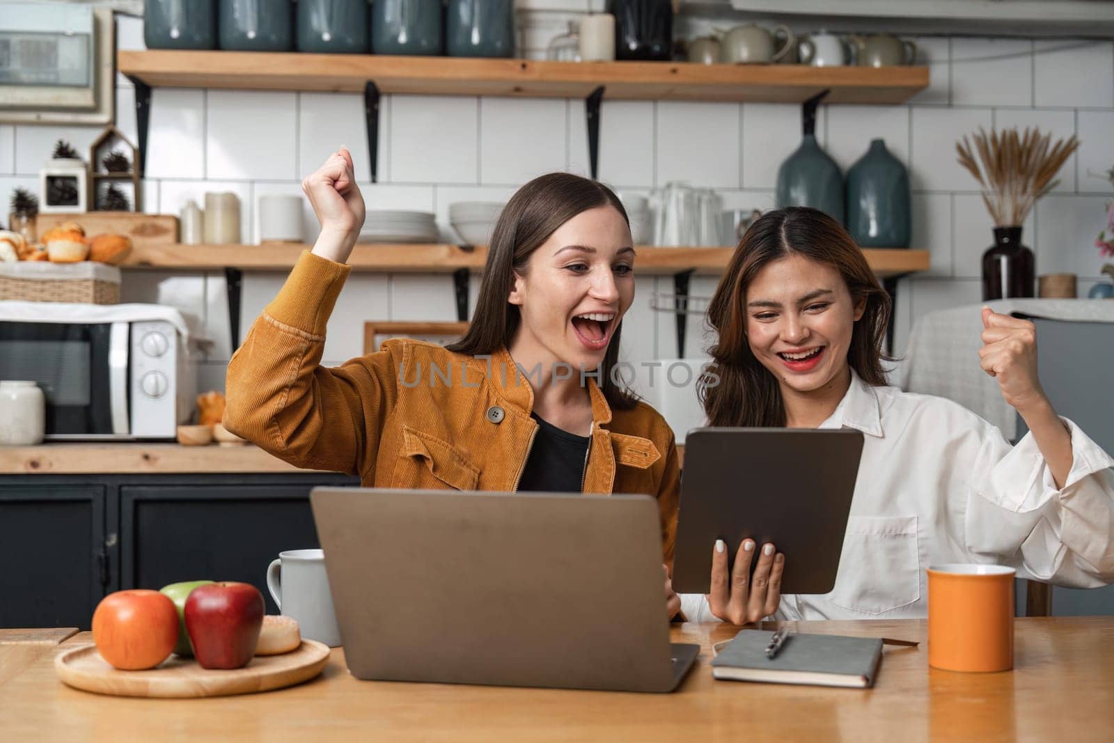 Two happy teenage girls Glad to raise your hand to receive message on tablet resting in kitchen.