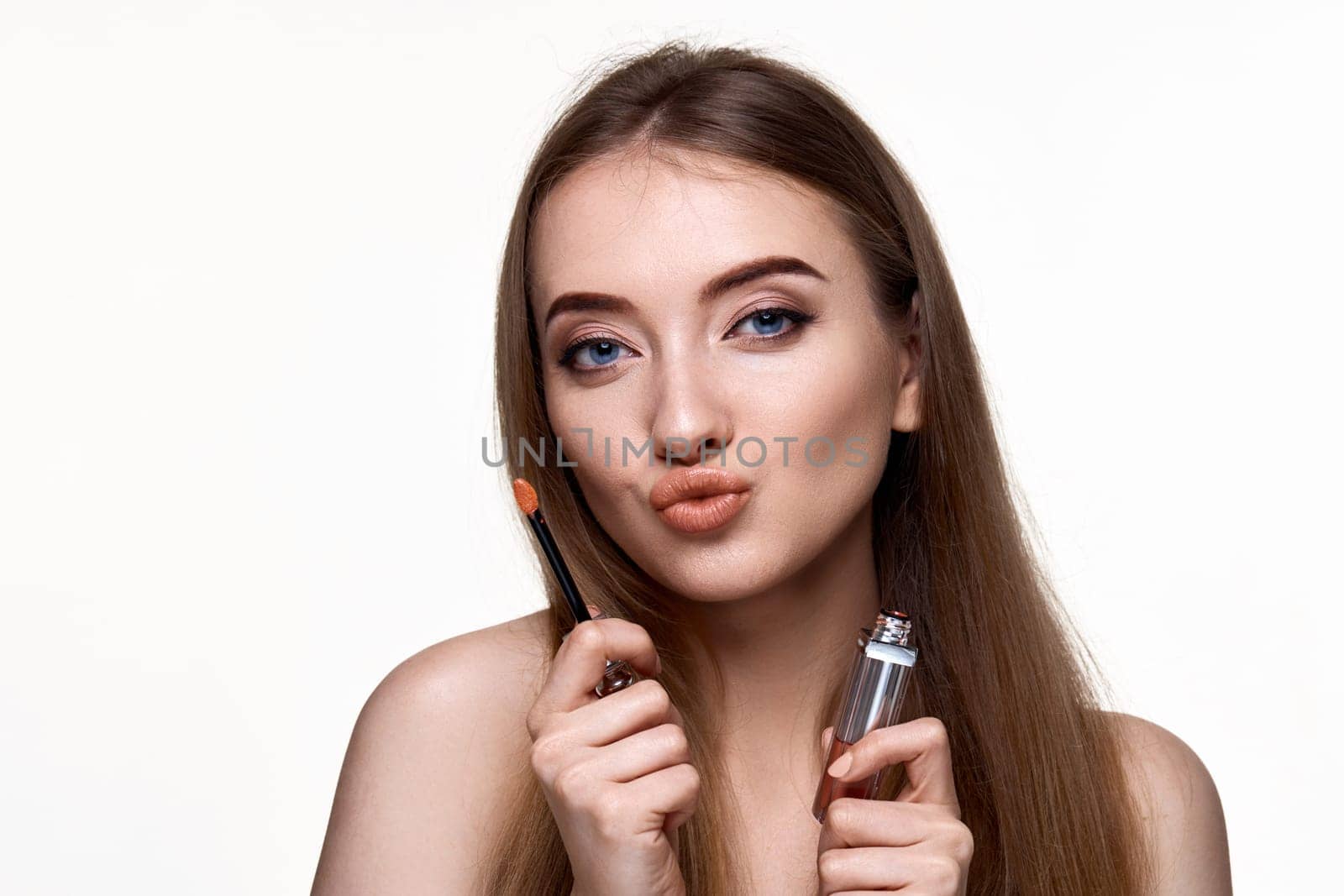 beautiful young woman with pouted lips holding lip gloss isolated on white background