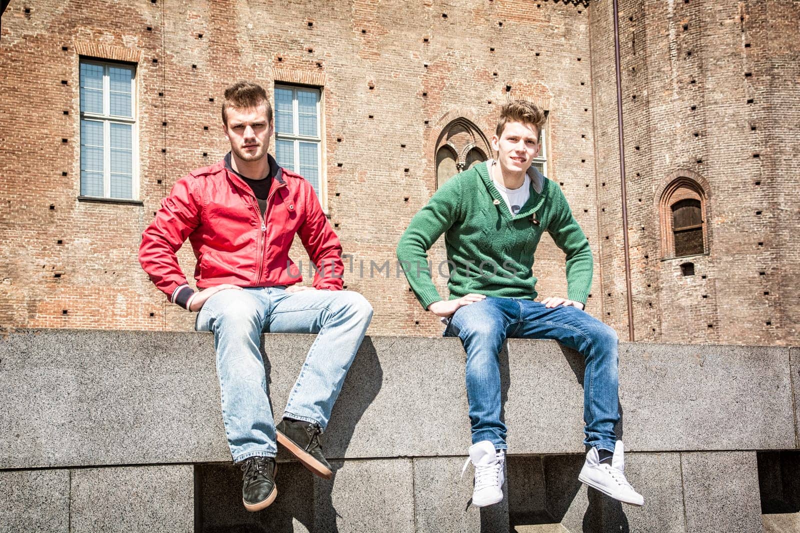 Two young men sitting on low wall in urban setting by artofphoto