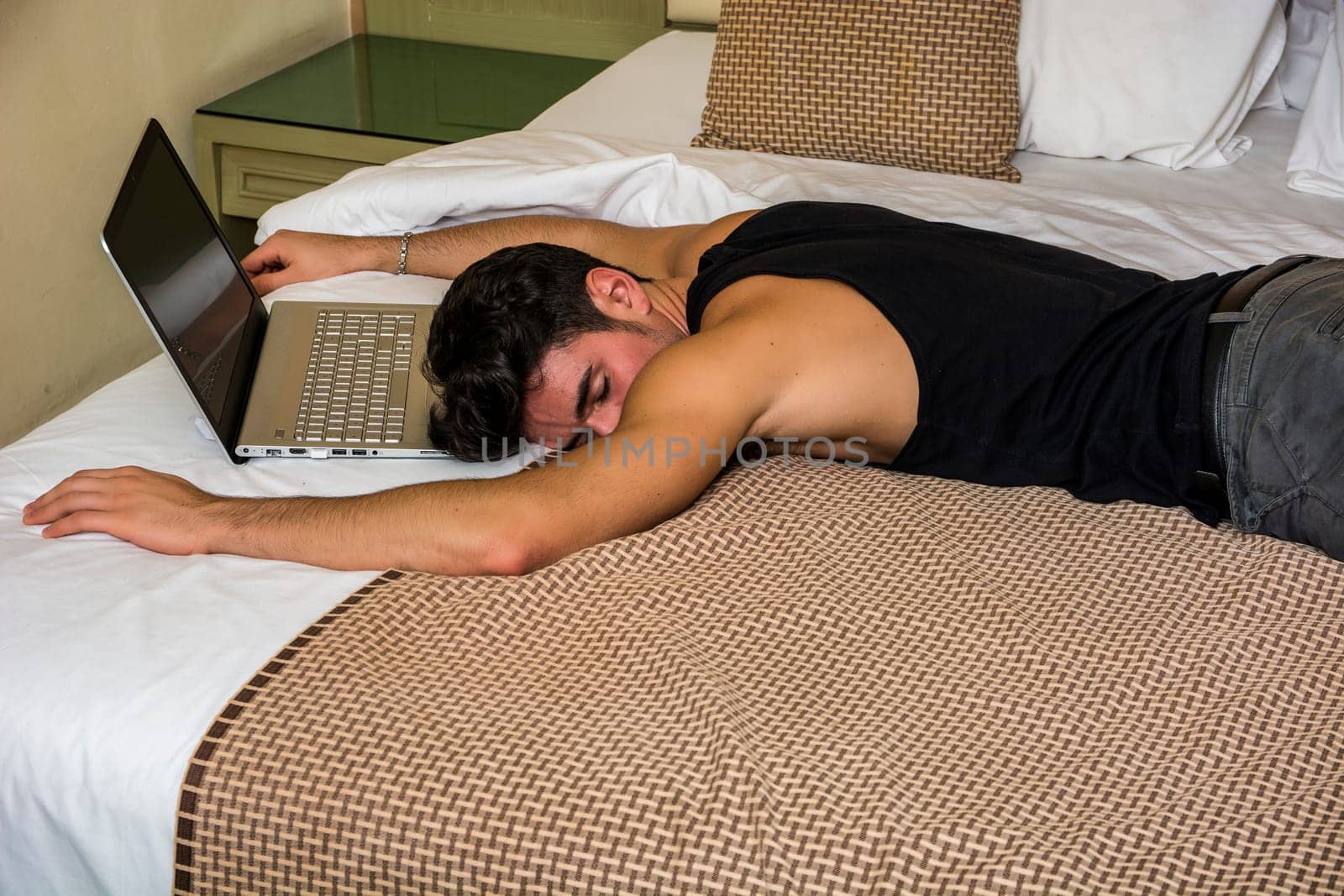 Close Up of Young Man with Dark Hair Sleeping on Bed Next to Laptop Computer and Cell Phone, Tired from Too Much Work