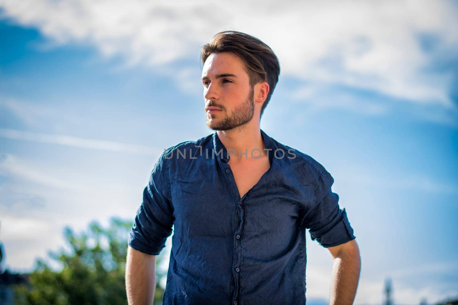 One handsome young man in urban setting in summer day, wearing blue shirt