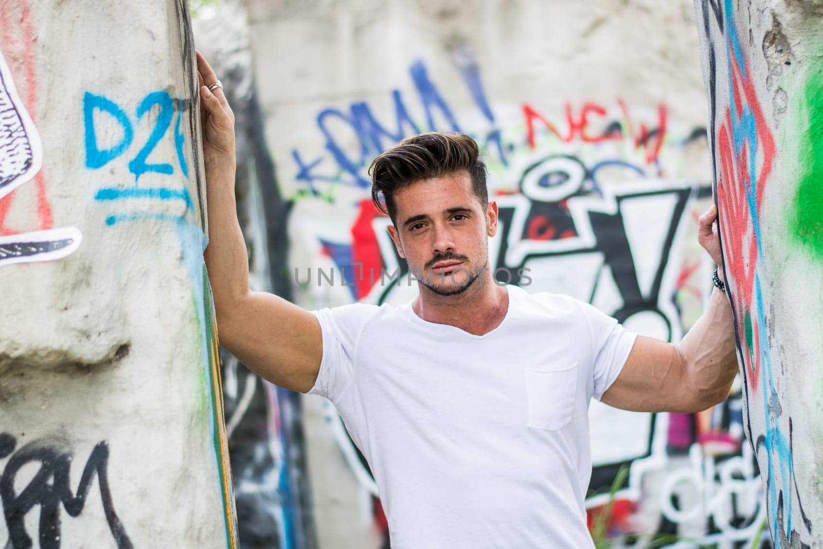 Handsome fit man in white t-shirt outdoor in city setting, looking at camera