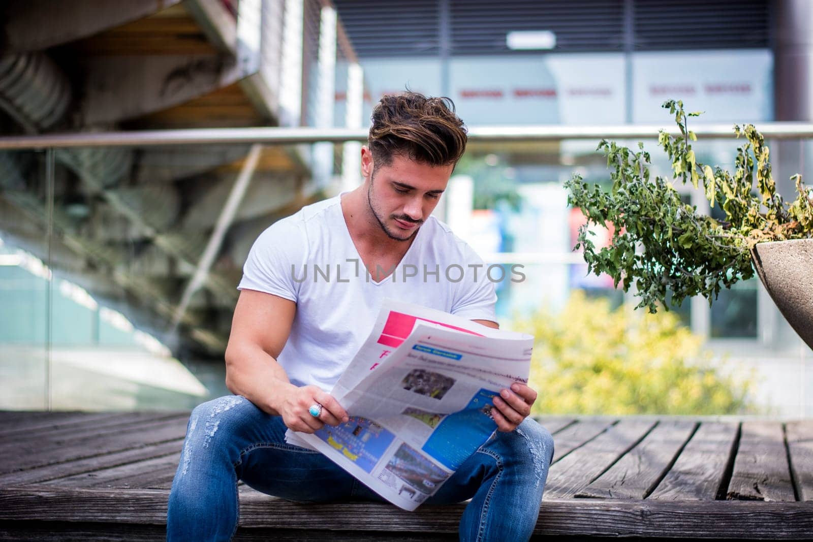 Handsome man reading newspaper outdoor in city setting, sitting on steps