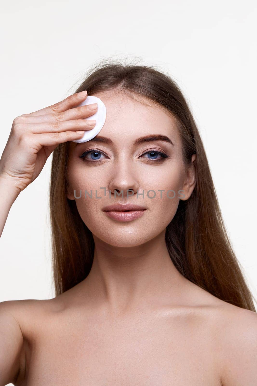 young woman holding white cotton pad for removing makeup isolated on white background