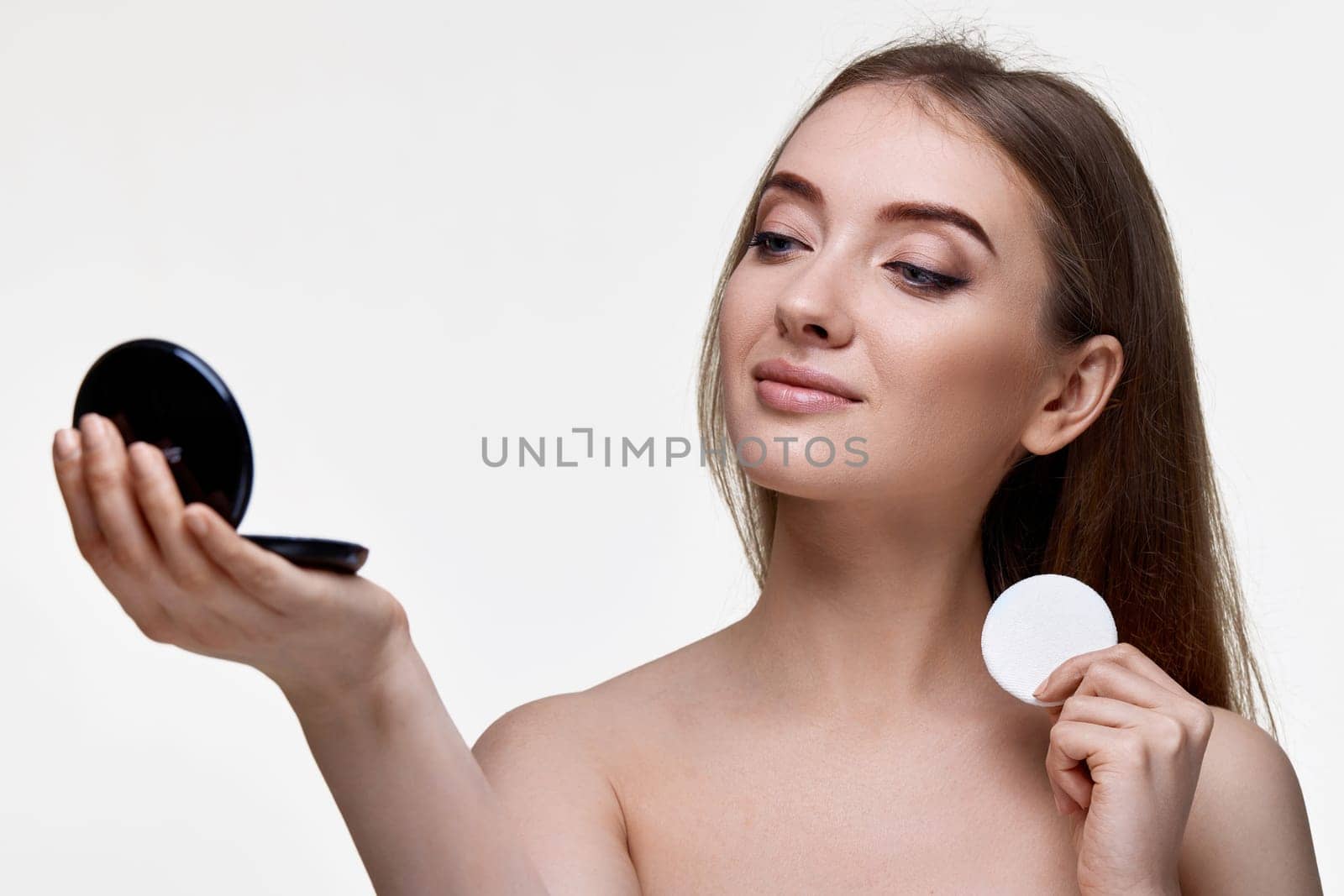beautiful young woman look at mirror and holding white cotton pad on white background