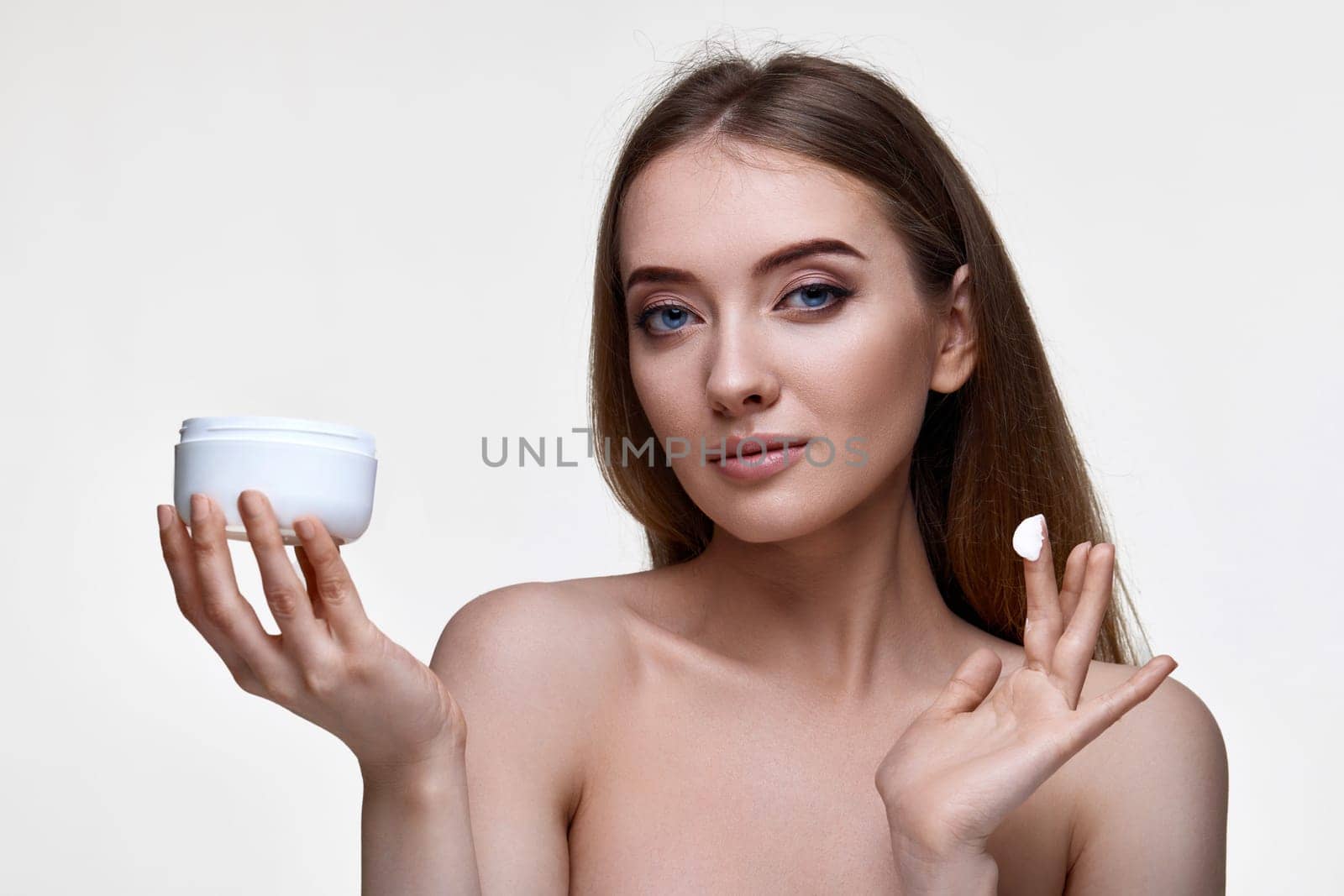 beautiful smiling young woman applying skin care cream on her face on white background