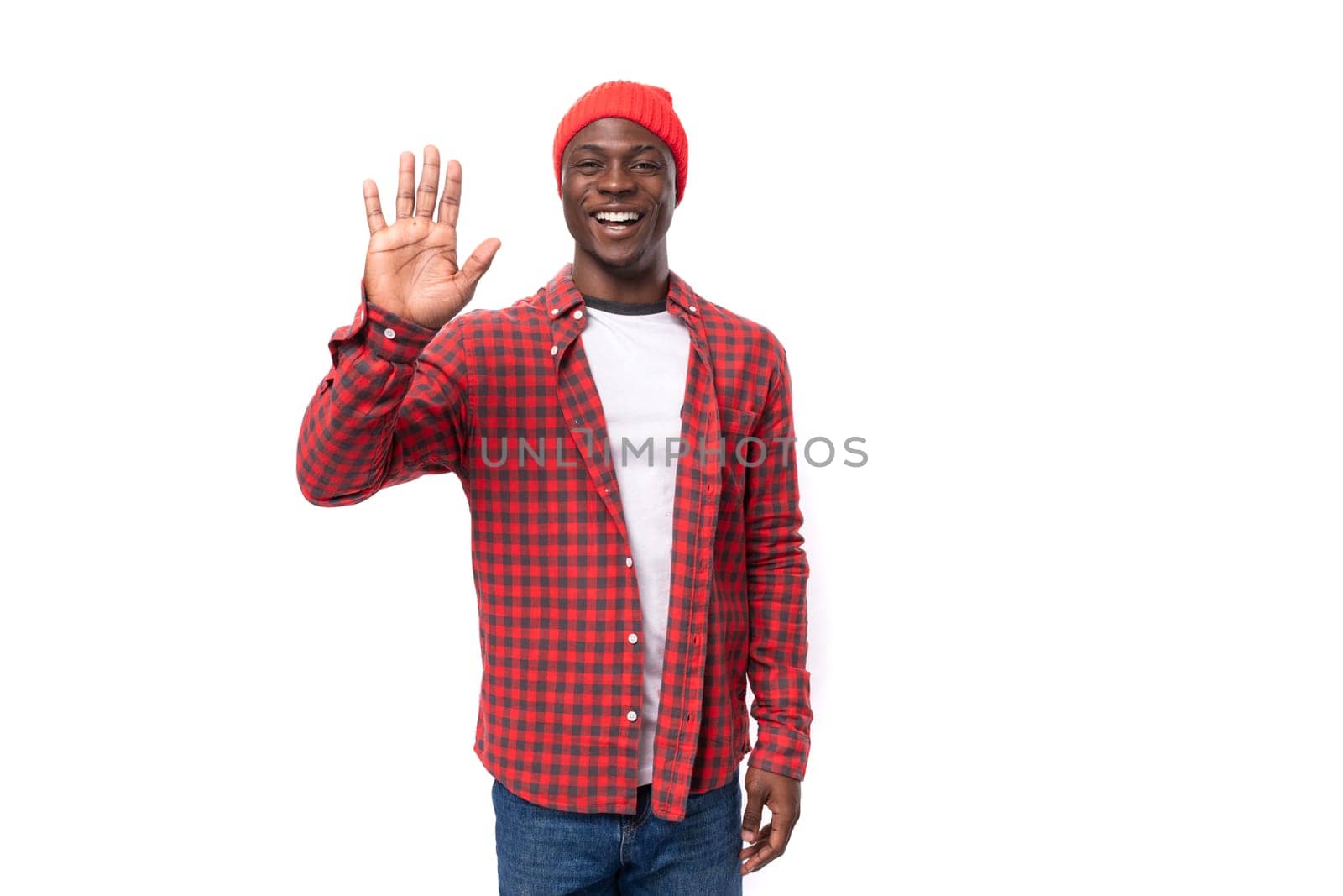 successful friendly handsome 30s black american man dressed in red shirt and cap waving hand on white studio background with copy space.