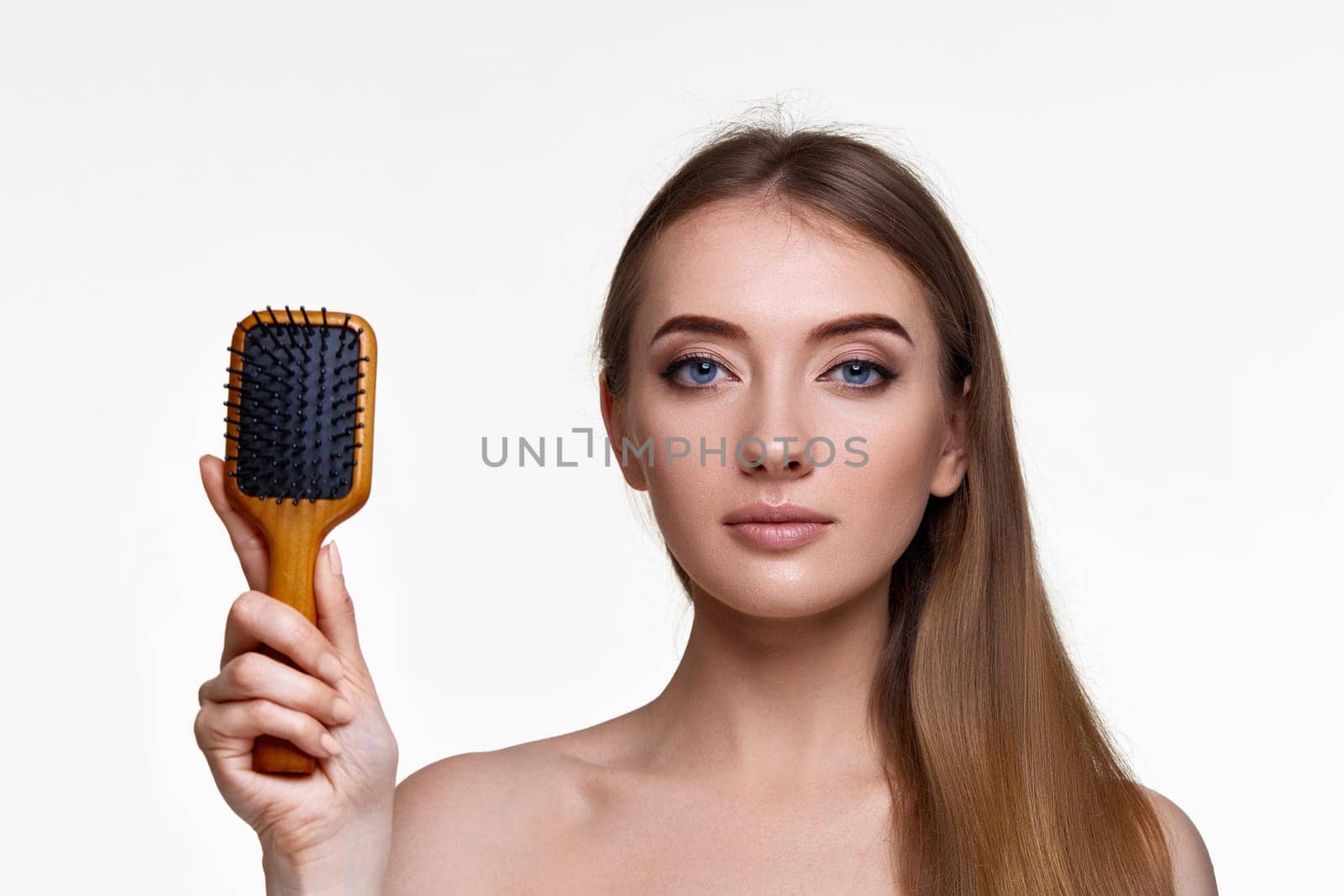 Beautiful brunette woman showing wooden brush and recommend haircare product for healthy long hair isolated on white background