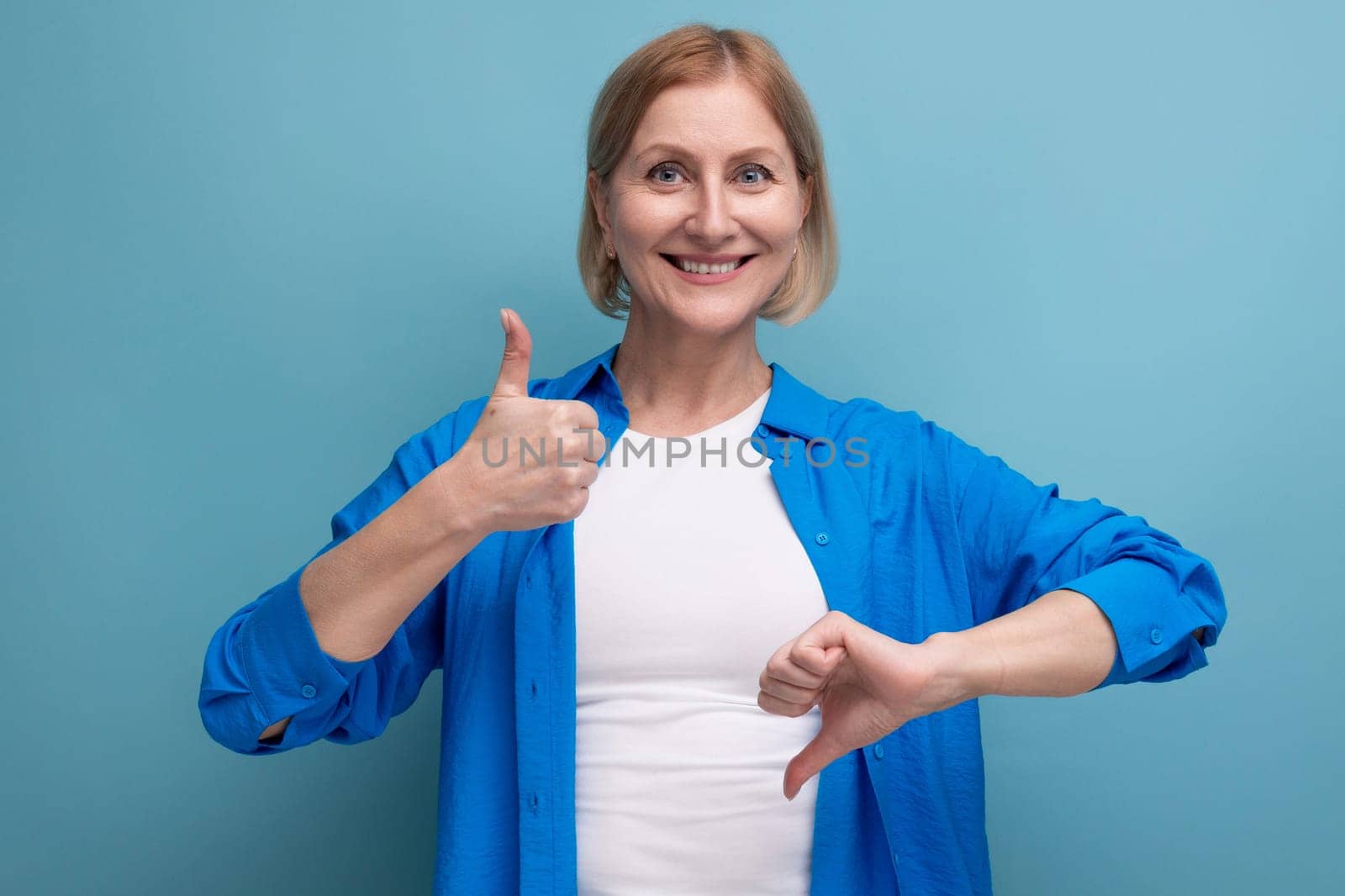 blonde 50s woman showing like and dislike on blue background with copyspace.