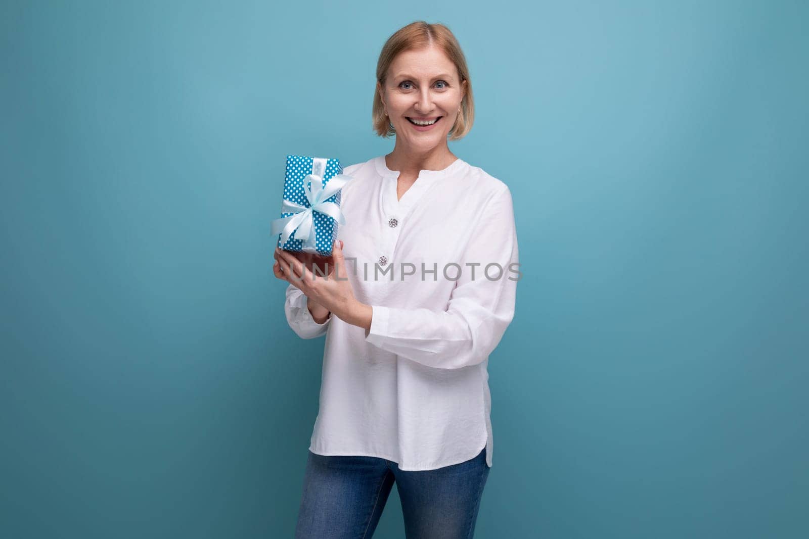 blond mature woman holding gift box on studio background.