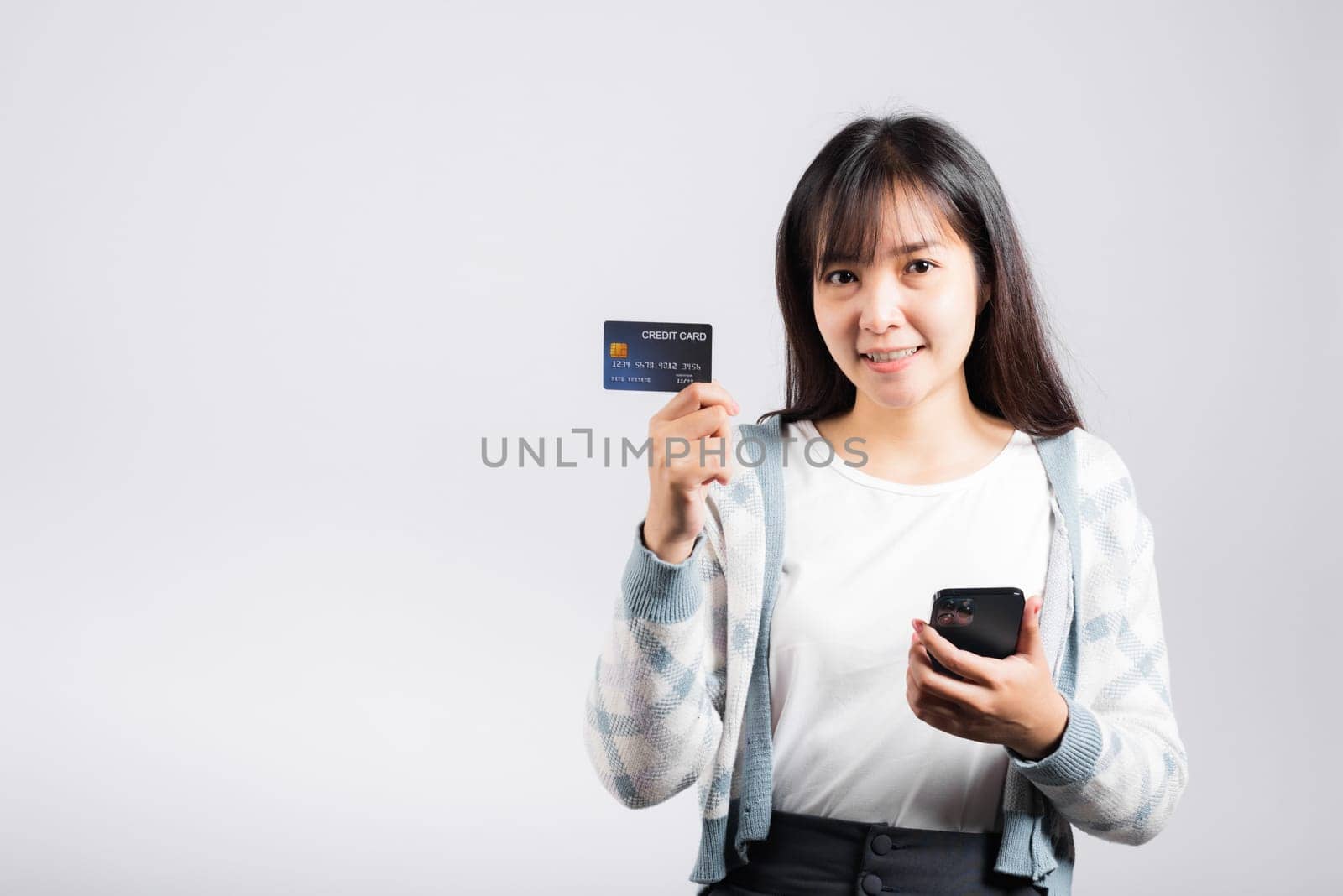 Woman excited smiling hold mobile phone and plastic debit credit bank card for payment studio shot isolated white background, happy young female using smartphone buy and pay online shopping