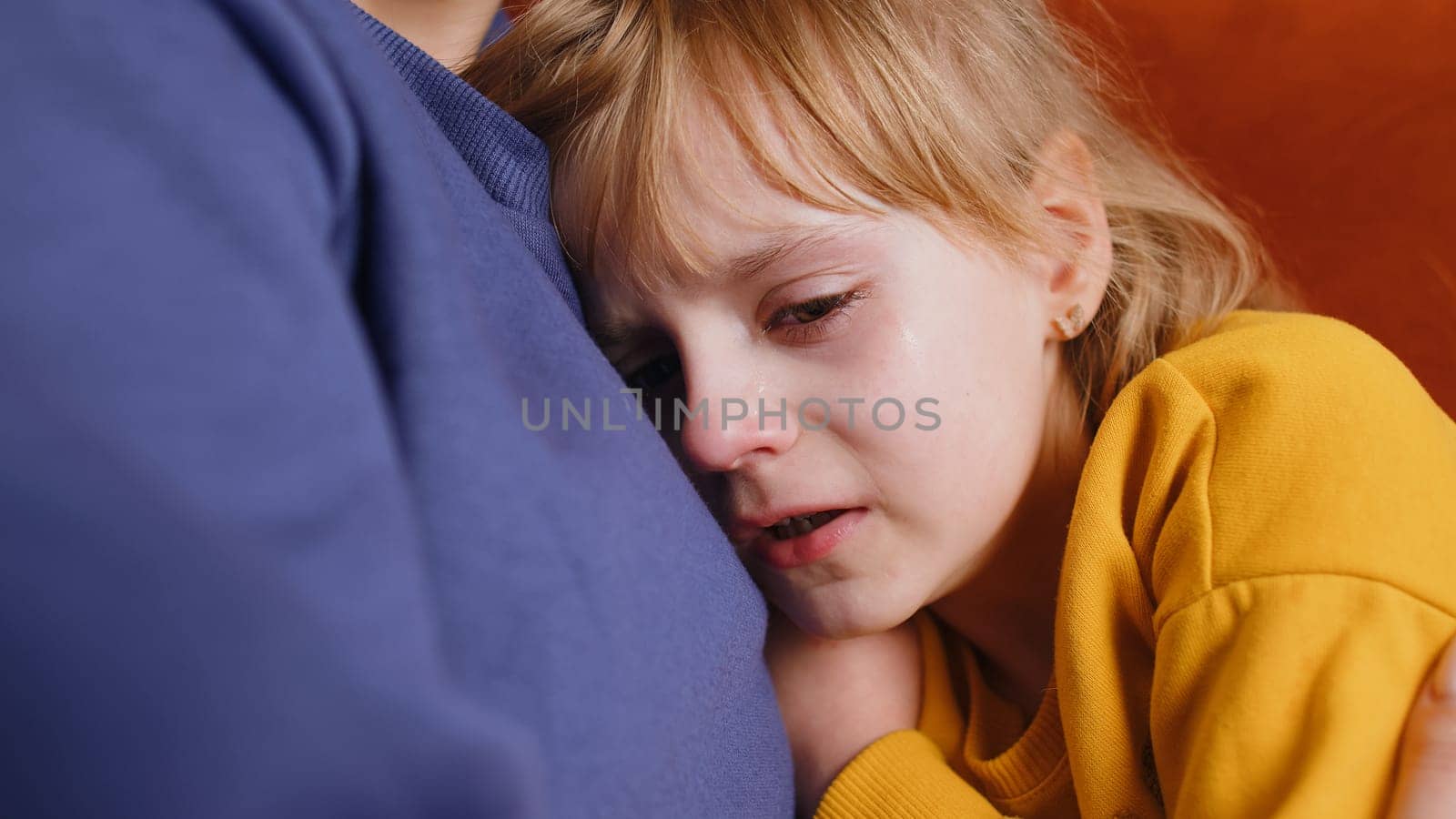 Close-up portrait of upset child little girl kid crying with tears flowing down on her cheek, toddler lies on mother at home. Mom hugs, embrace, takes pity on her daughter. Quarrel, bullying at school