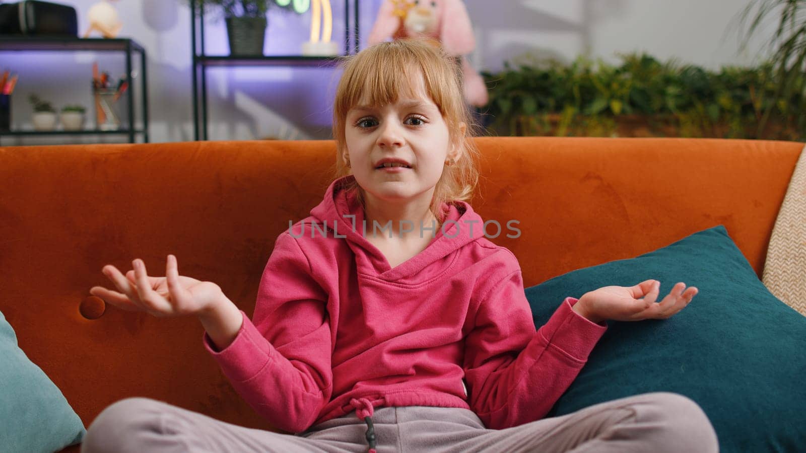 What. Why. Young child kid girl raising hands in indignant expression, asking reason of failure, demonstrating disbelief irritation by troubles. Female teen toddler at home in living room sits on sofa
