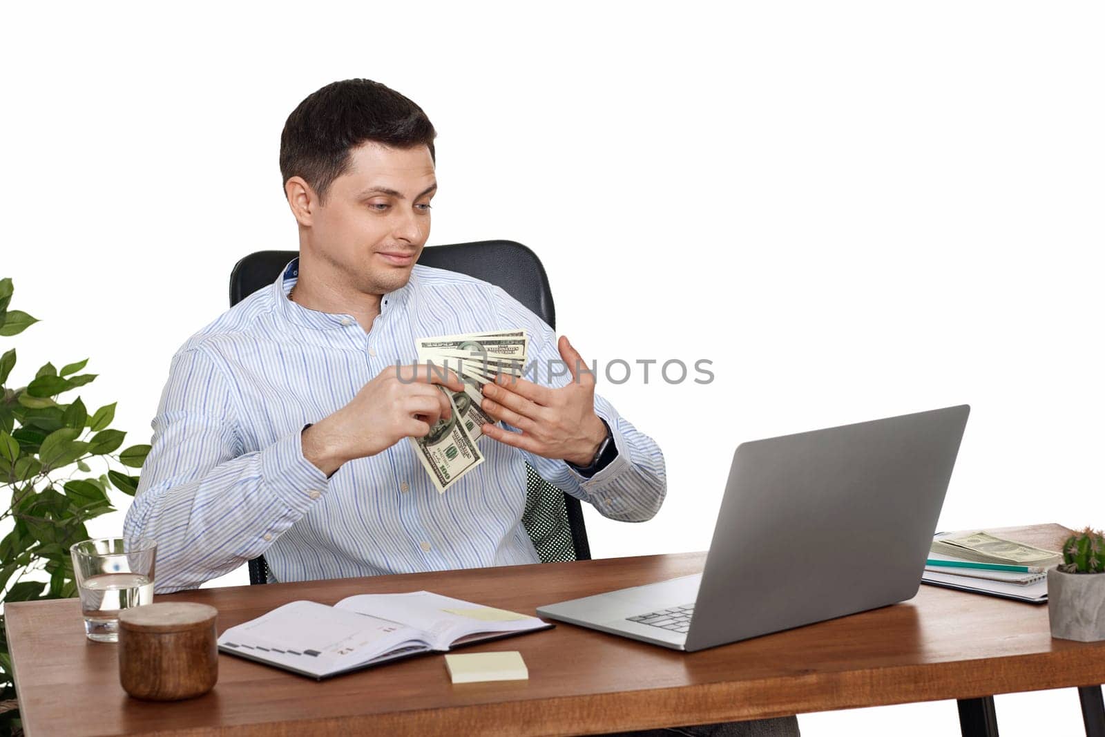 young handsome businessman working on laptop and holding money while sitting on chair at desk.