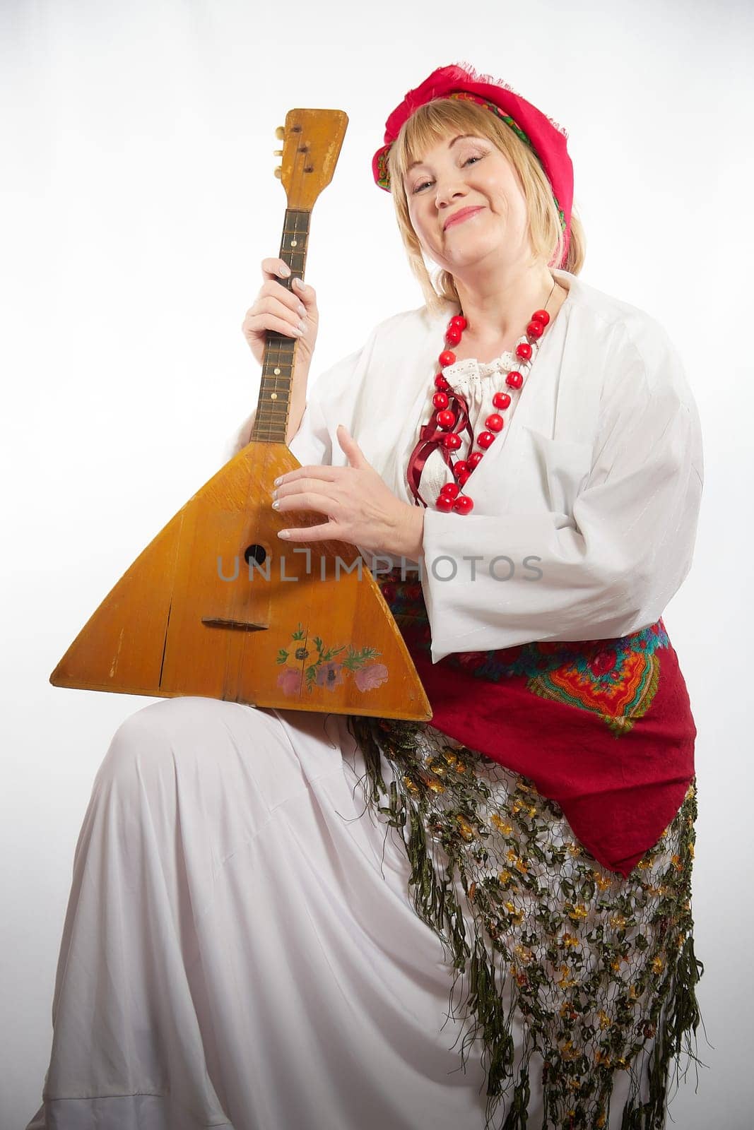 Cheerful funny adult mature woman solokha with musical balalaika. Female model in clothes of national ethnic Slavic style. Stylized Ukrainian, Belarusian or Russian woman poses in a comic photo shoot by keleny