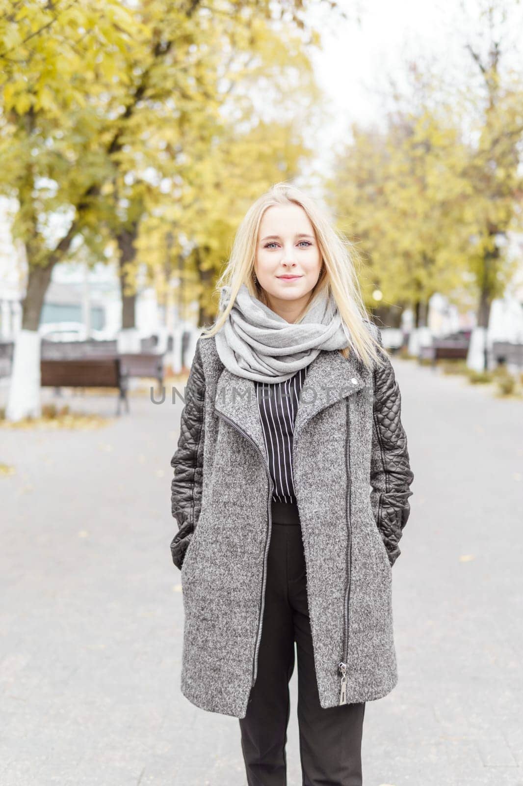 A young blonde walks through the autumn city in a gray coat. The concept of urban style and lifestyle