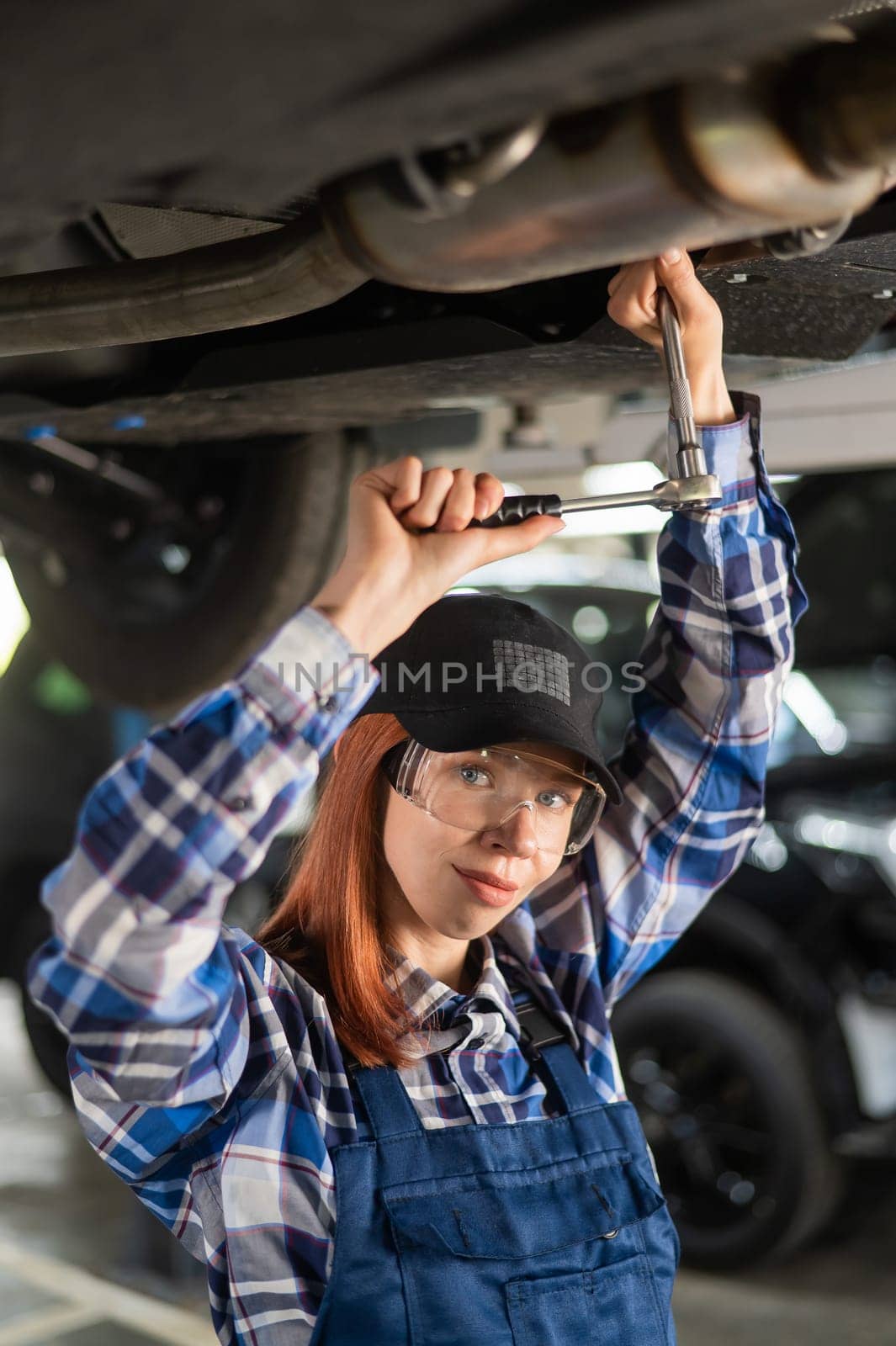 Female mechanic unscrew the nuts on the bottom of the car that is on the lift. A girl at a man's work