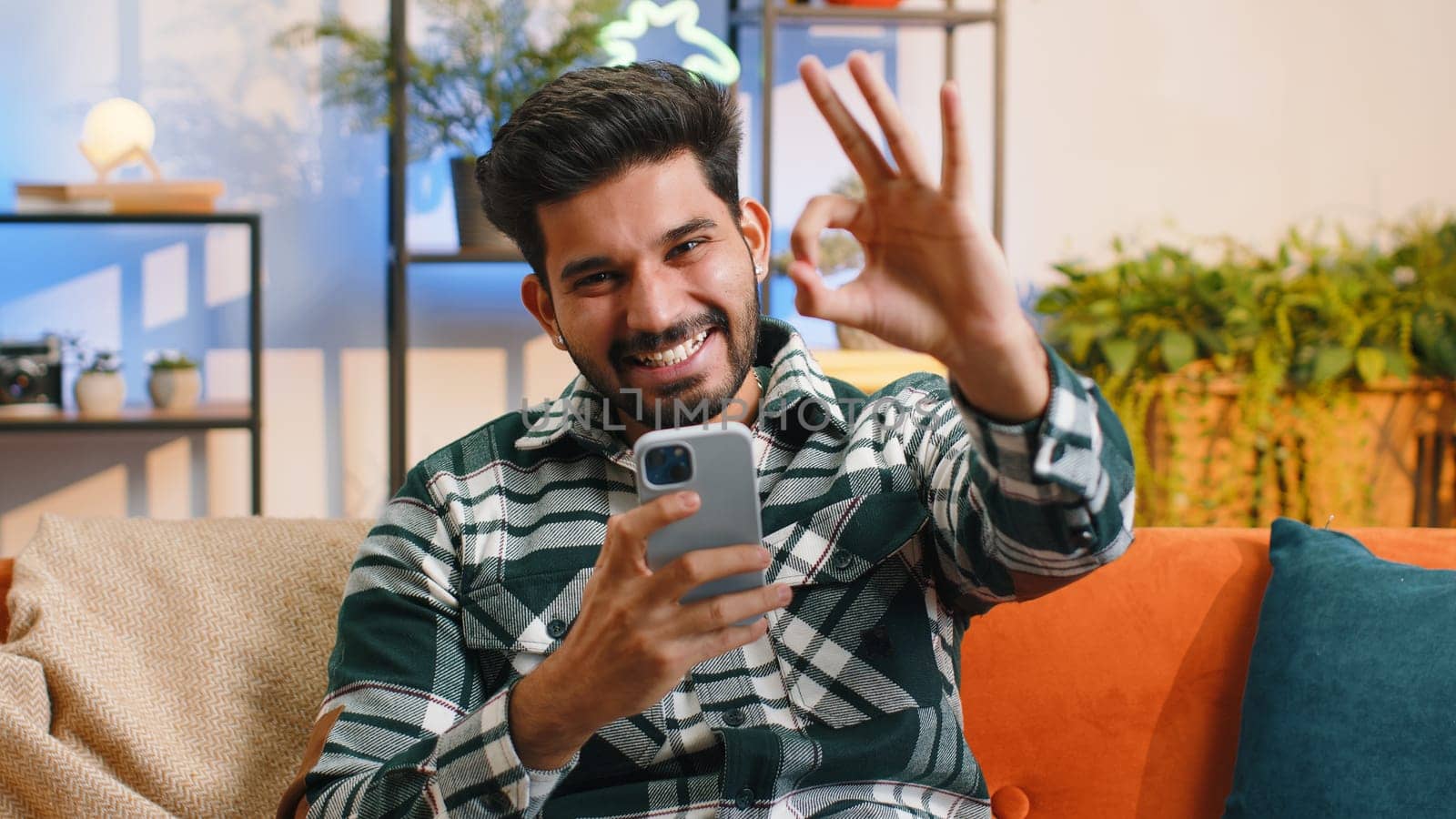 Happy indian man use mobile smartphone typing browsing say Wow yes found out great big win good news celebrate lottery jackpot doing winner gesture. Hindu young guy at home in room sitting on sofa