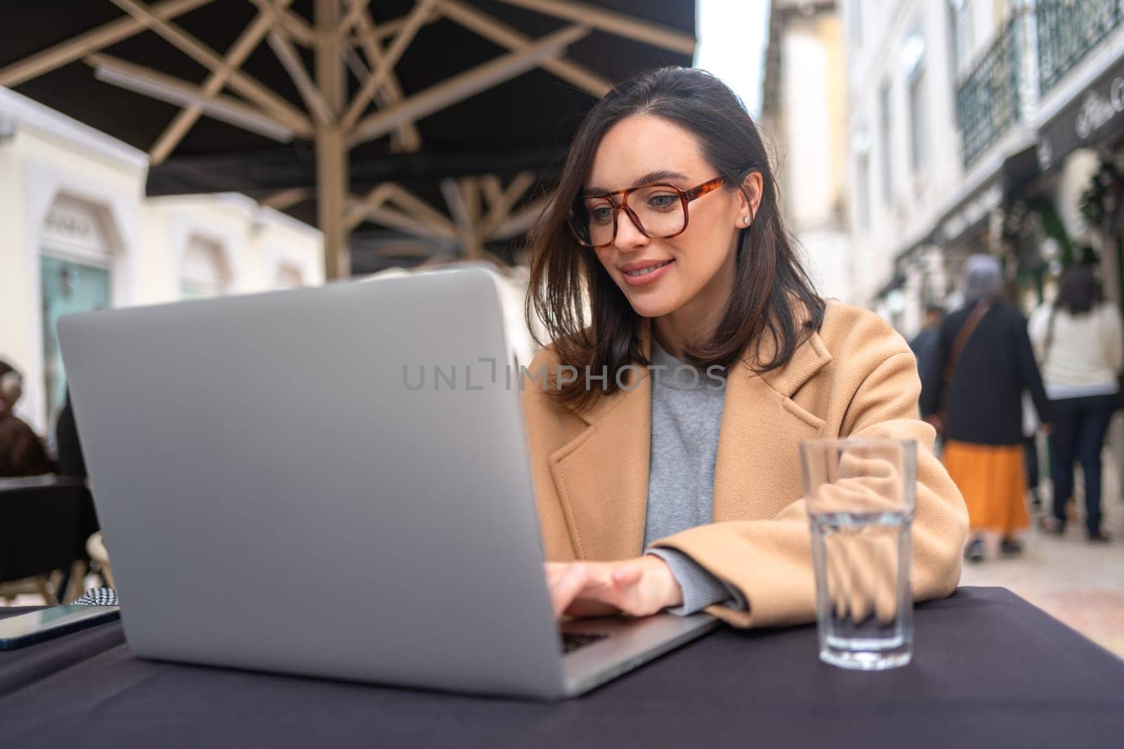 Photo portrait of smiling adorable girl typing on laptop browsing web drinking water in restaurant outdoors