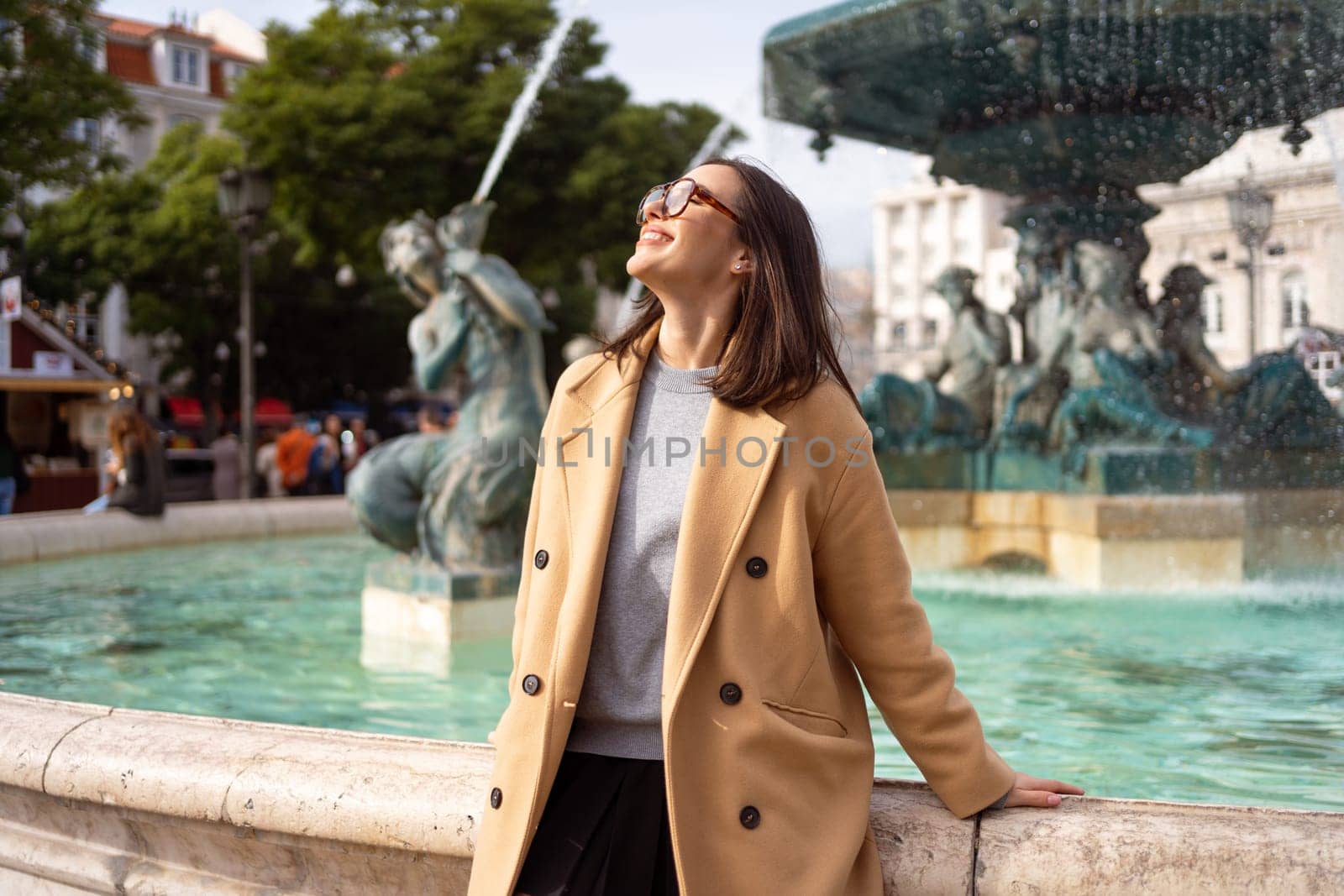 Female tourist enjoying in Lisbon downtown, Portugal. Sunny day. Travel Europe concept. woman dressed stylish coat sitting in front of baroque fountains in Praca Dom Pedro IV or Rossio Square, Lisbon.