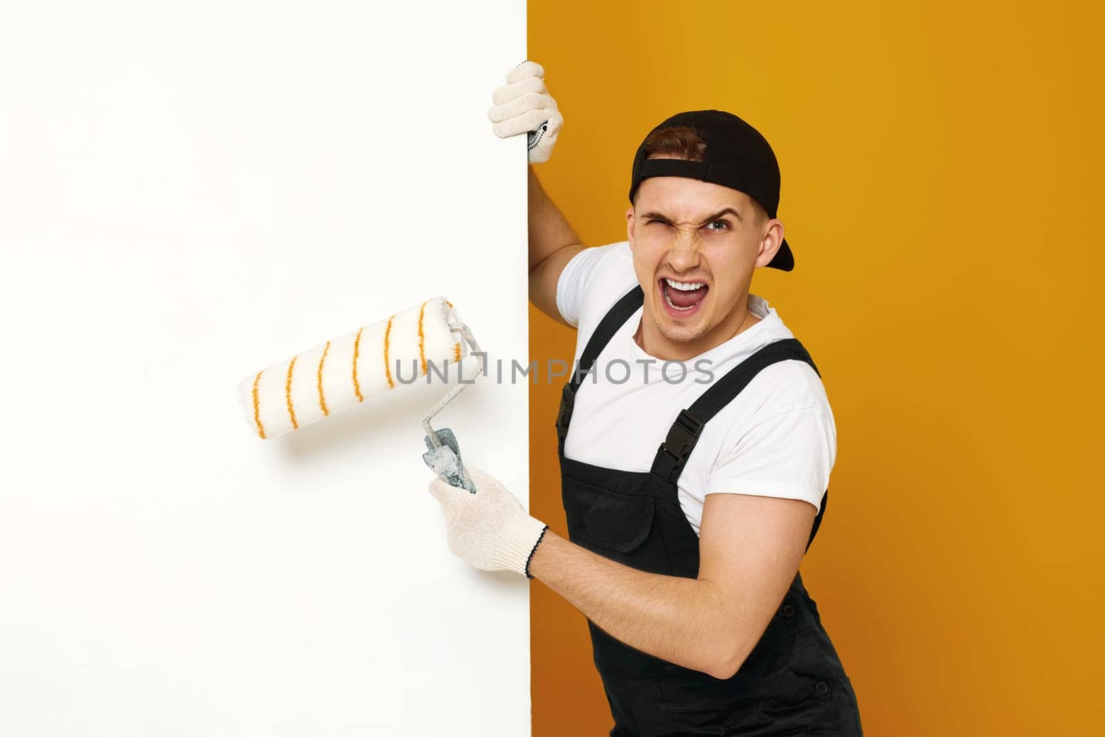 very excited man in working clothes painting white walls in the room. copy space for text