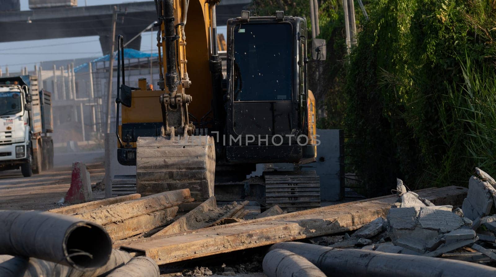 Yellow digger parked at construction site with blur truck driving on the road and housing estate construction project. Backhoe after work. Earth moving machine at construction site of housing estate. by Fahroni