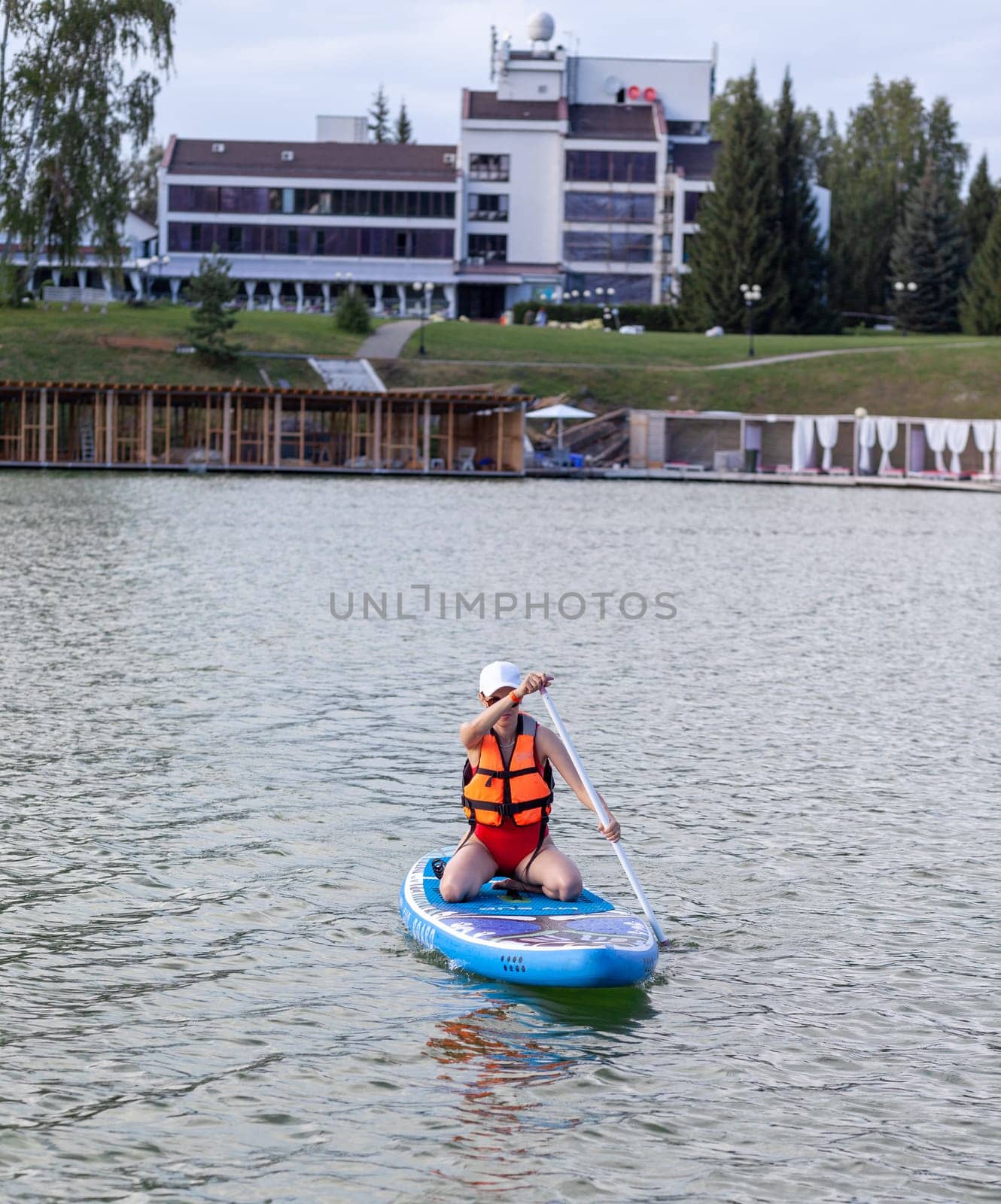 A girl in a life jacket swims on a SUP board. SUP board Stand up paddle girl boarding on lake standing happy on blue water.