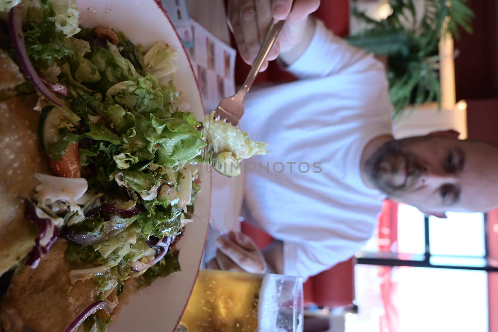 Close-up portrait of a man eating salad with tomatoes on the red brick wall background. Healthy and vegan food concept.