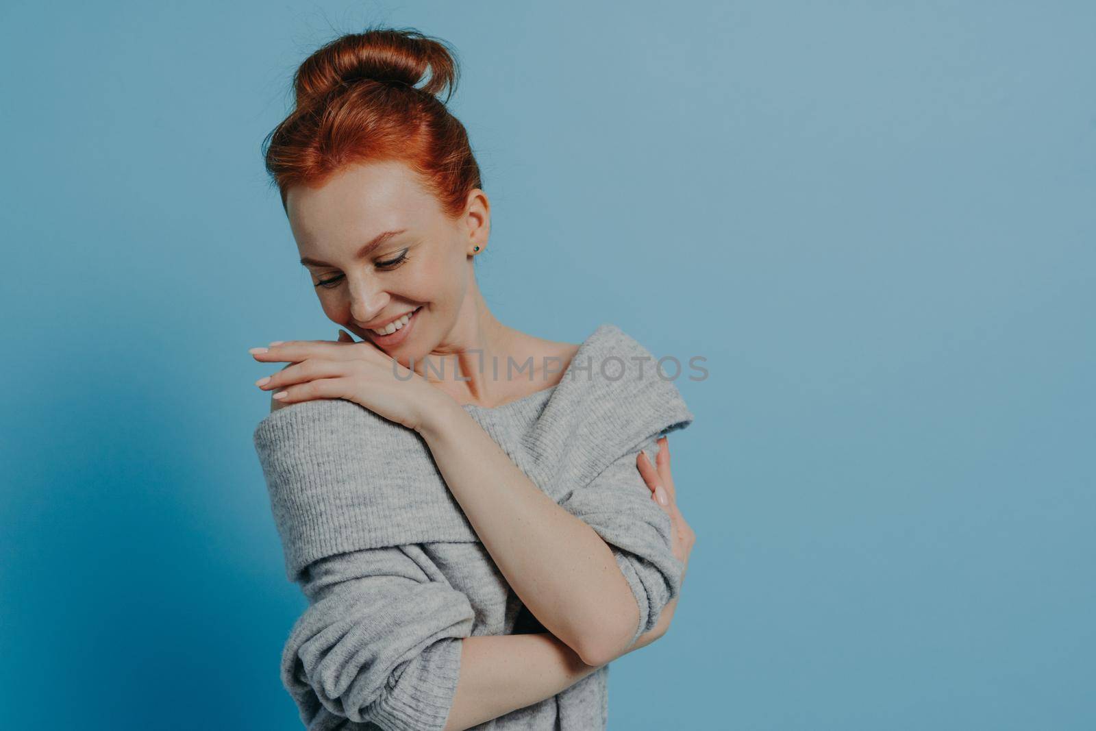 Young beautiful romantic red-haired woman wearing knitted sweater embracing herself with pleasure by vkstock