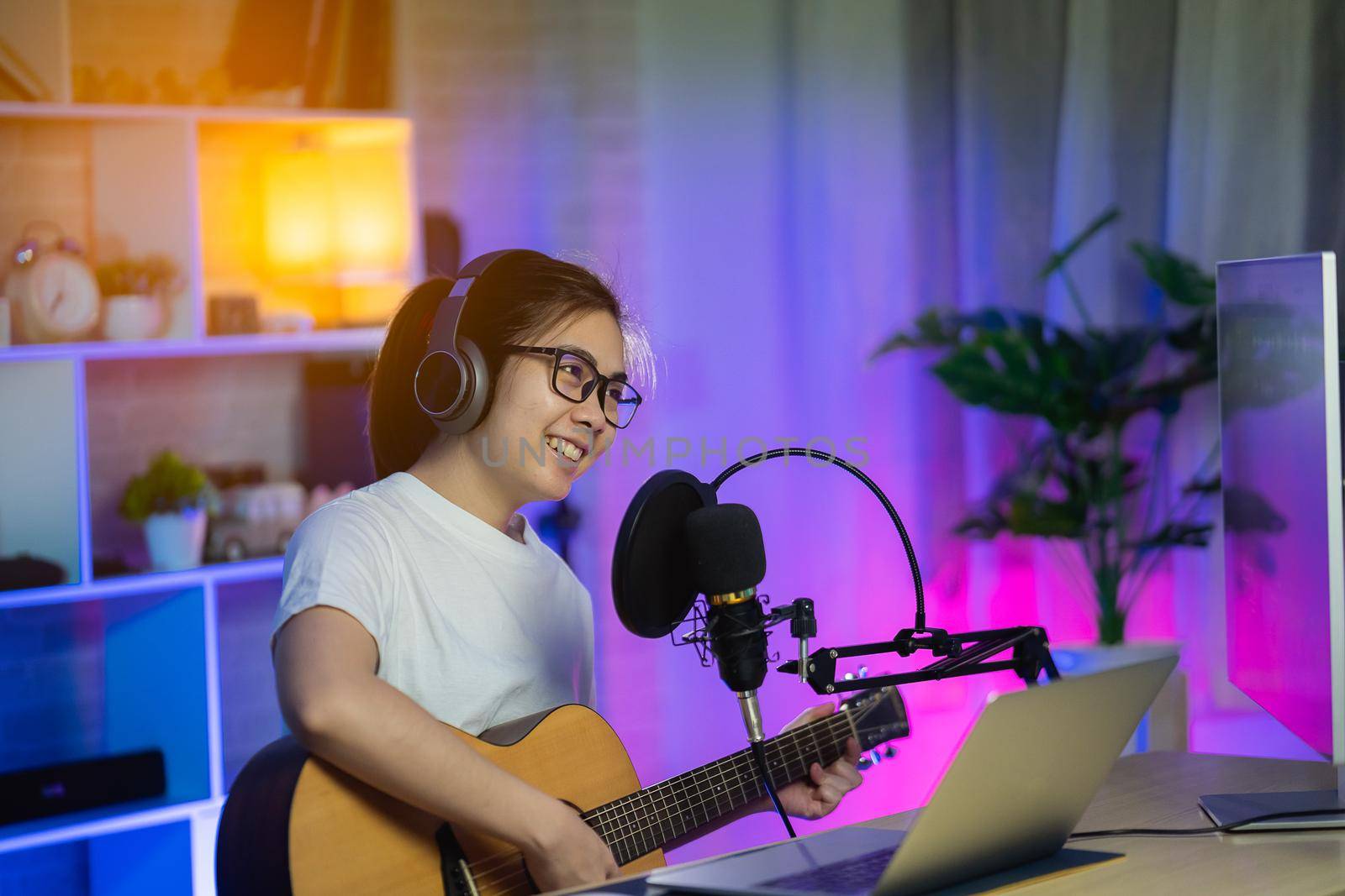 Beautiful girl singing with headphone and playing guitar recording new song with microphone in the home recording studio by Wmpix