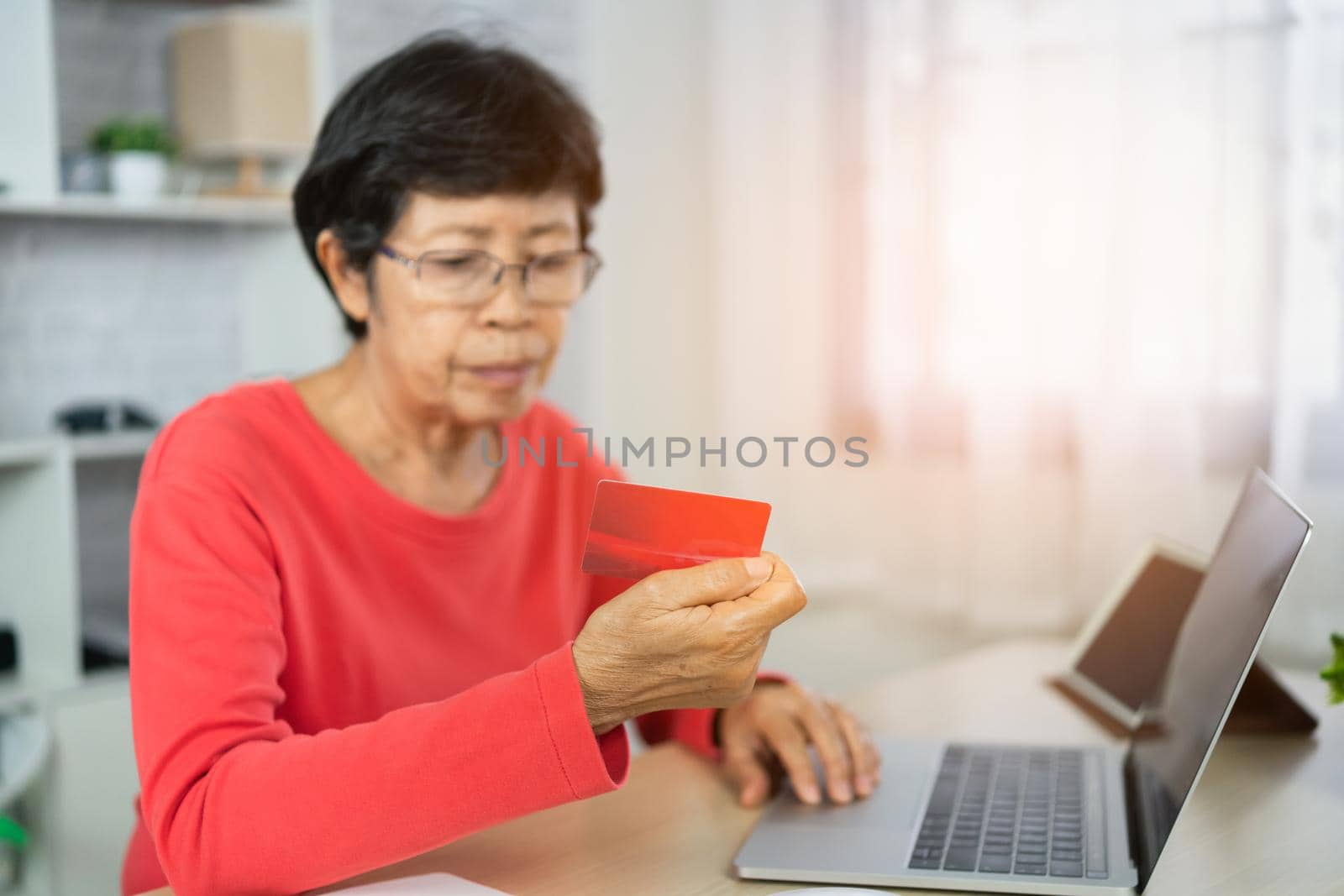senior women looking for credit card and using laptop shopping online by Wmpix