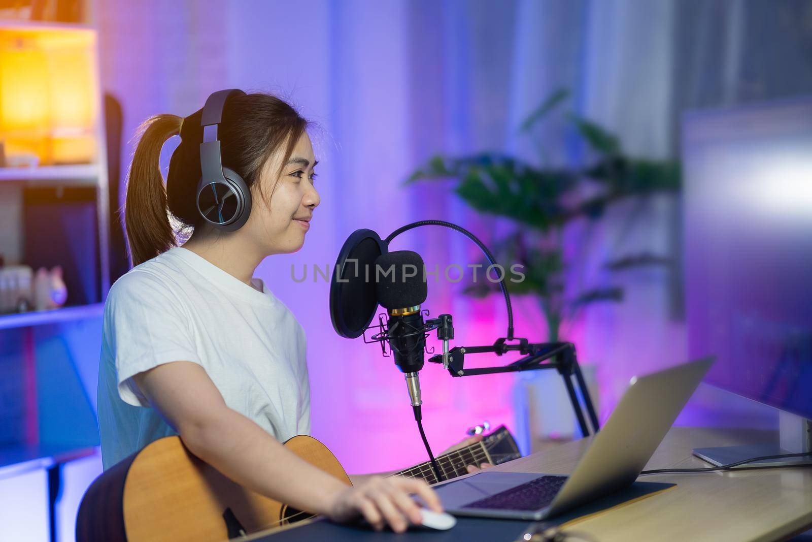 Beautiful girl singing with headphone and playing guitar recording new song with microphone in the home recording studio by Wmpix