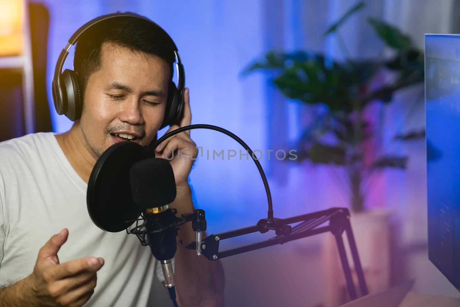 Man singing with headphone recording new song with microphone in the home recording studio by Wmpix