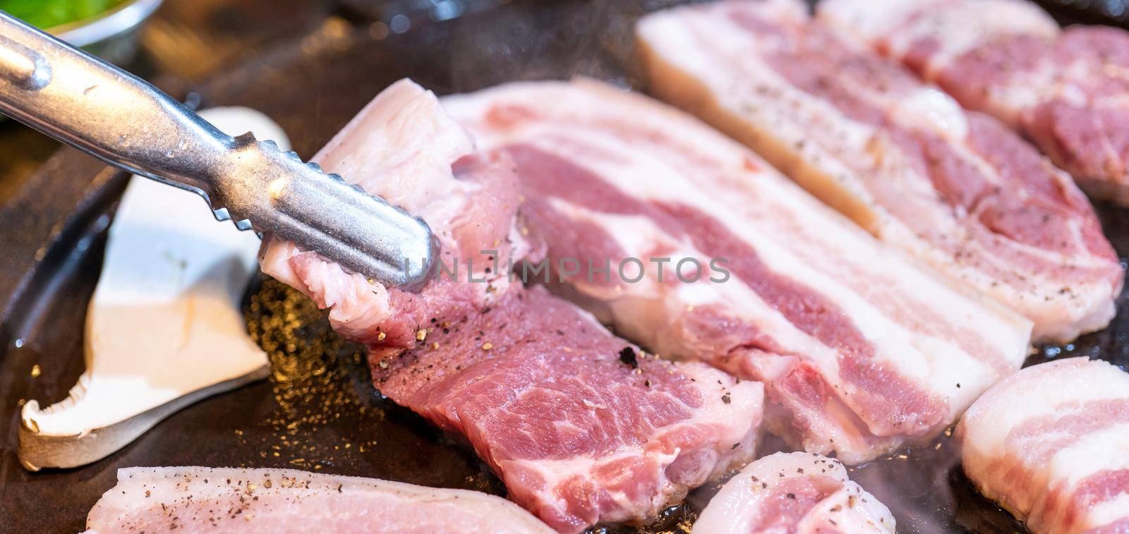 Pan-fried black pork meal in Korea restaurant, fresh delicious korean food cuisine on iron plate with lettuce, close up, copy space, lifestyle by ROMIXIMAGE