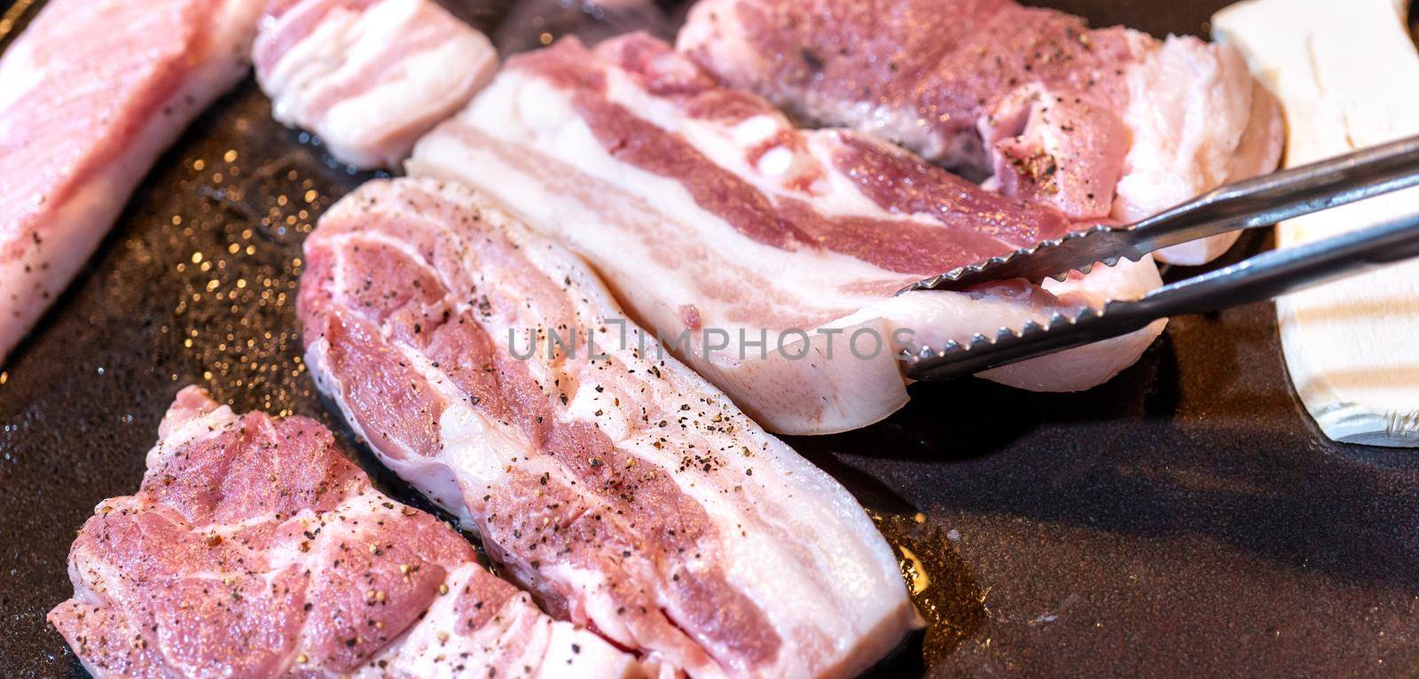 Pan-fried black pork meal in Korea restaurant, fresh delicious korean food cuisine on iron plate with lettuce, close up, copy space, lifestyle by ROMIXIMAGE